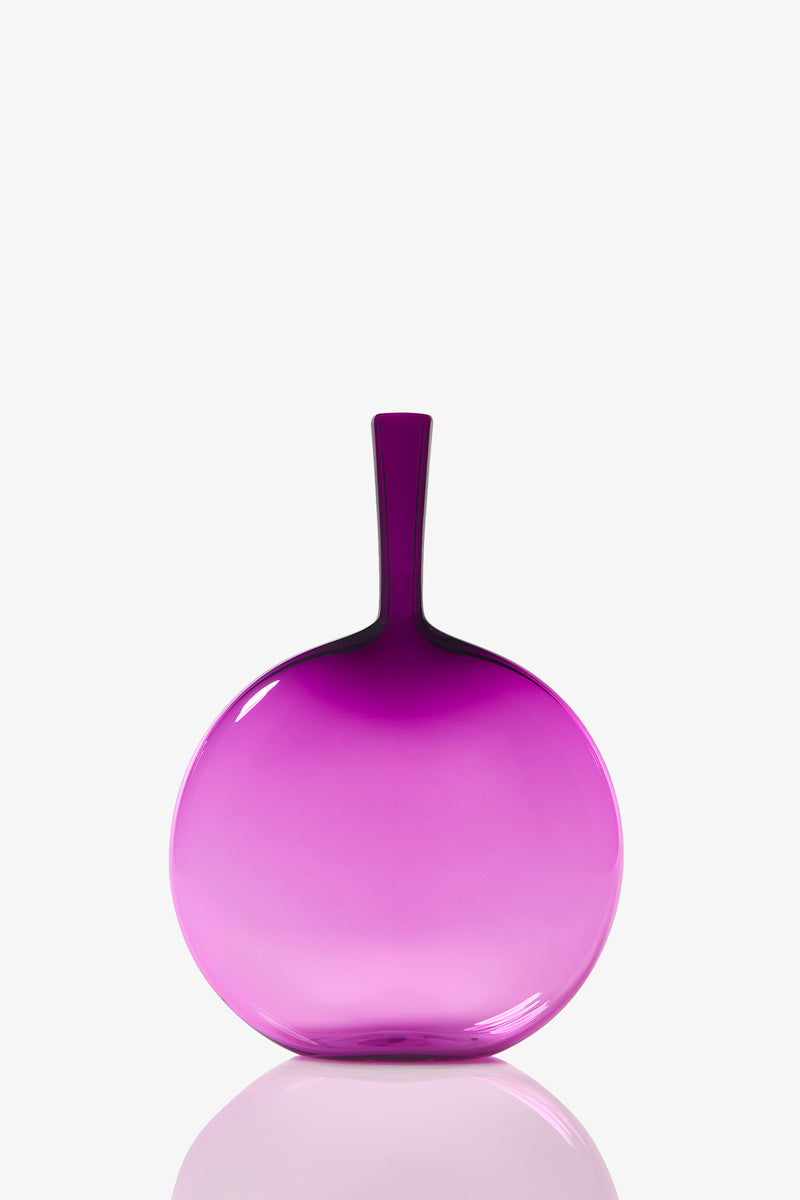 The Flask Angelic Bottle is a round, flat glass vase with a narrow neck. It features a gradient design, fading from deep purple at the top to light pink at the bottom, and rests on a white surface.