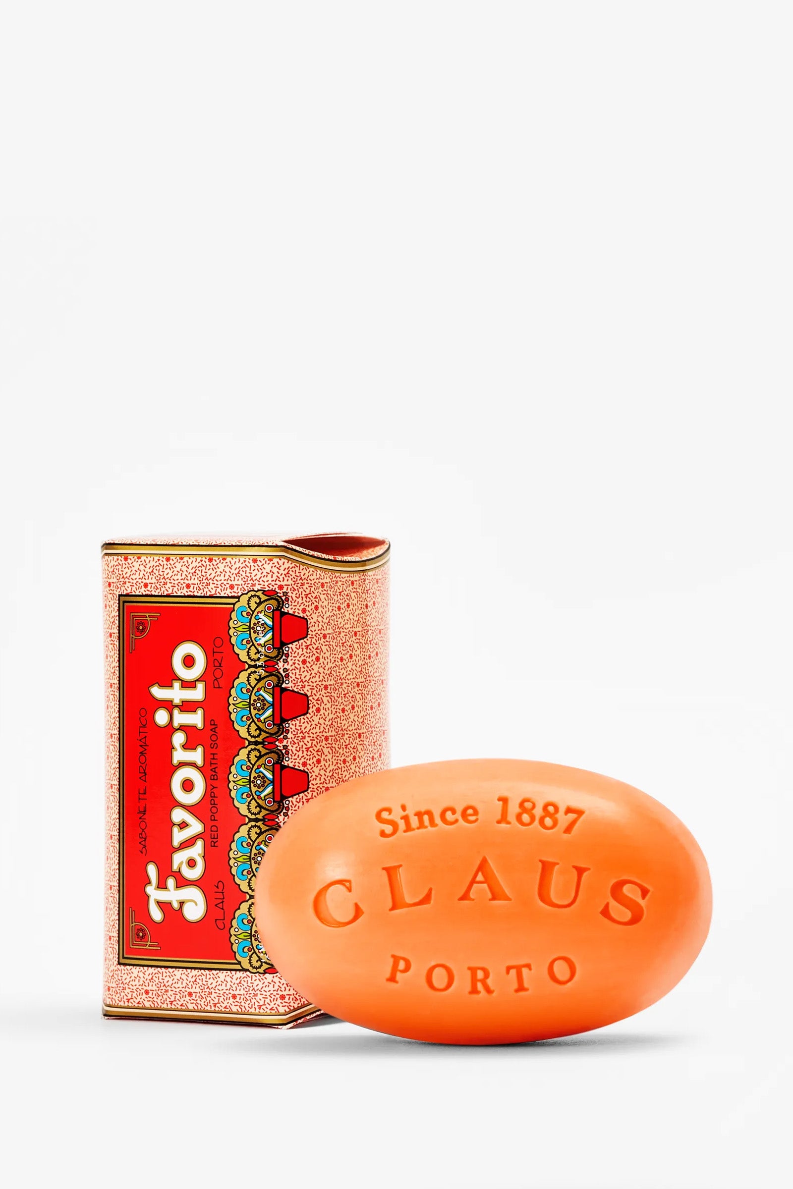 A vibrant orange bar of Claus Porto Favorito Soap, embossed with “Since 1887 CLAUS PORTO,” is displayed beside its ornate red and gold Favorito box.