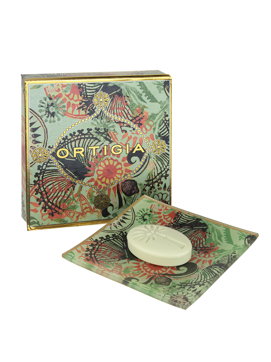 The Ortigia Fico D'India Soapplate features a green, oval embossed soap bar in a matching glass soap dish with a colorful patterned box, all set against a white background.