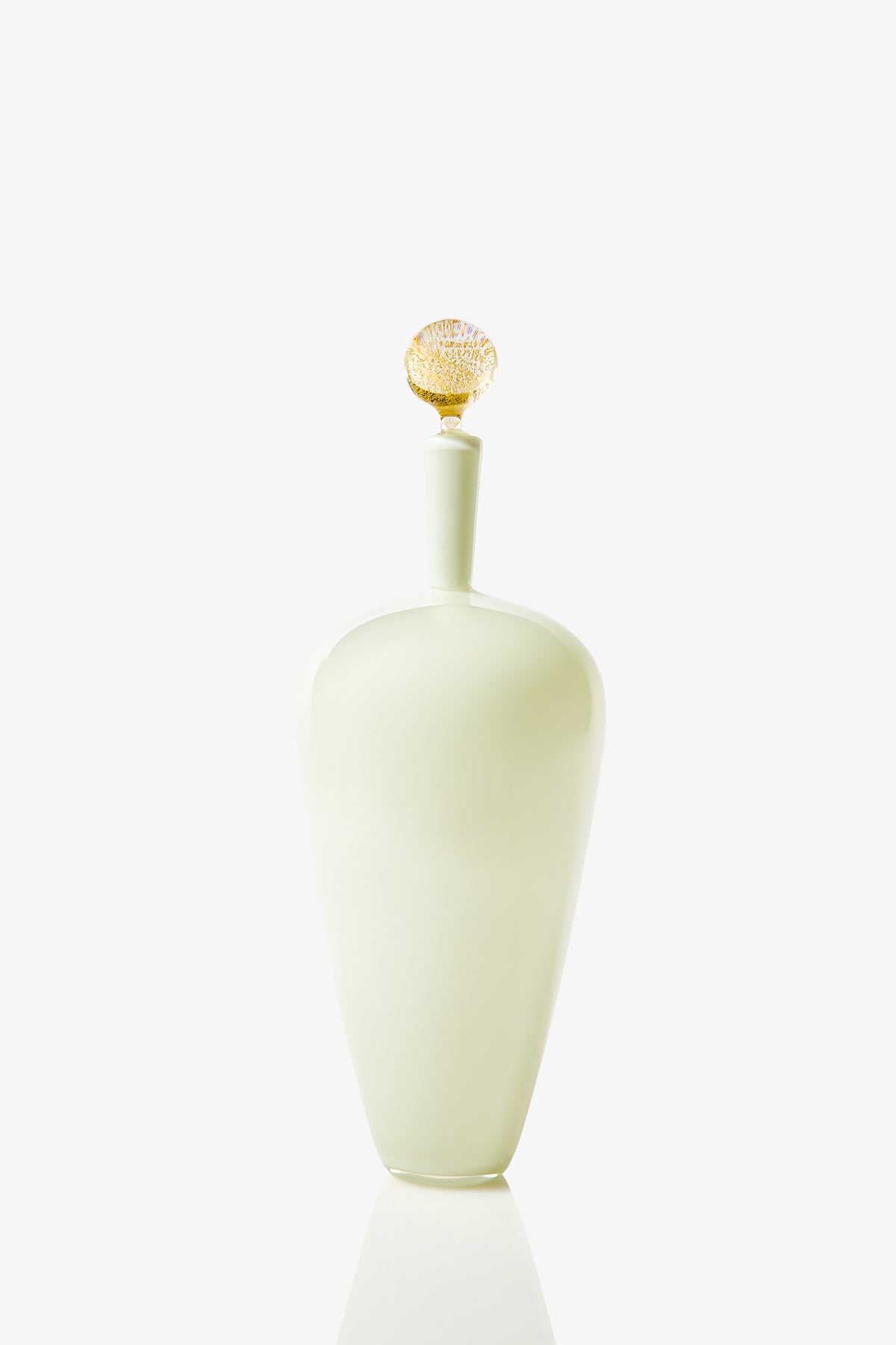 The High Shoulder Carmella Barware features a tall, elegant pale green glass bottle with a rounded body and narrow neck, finished with a decorative textured gold stopper, displayed against a plain white background.
