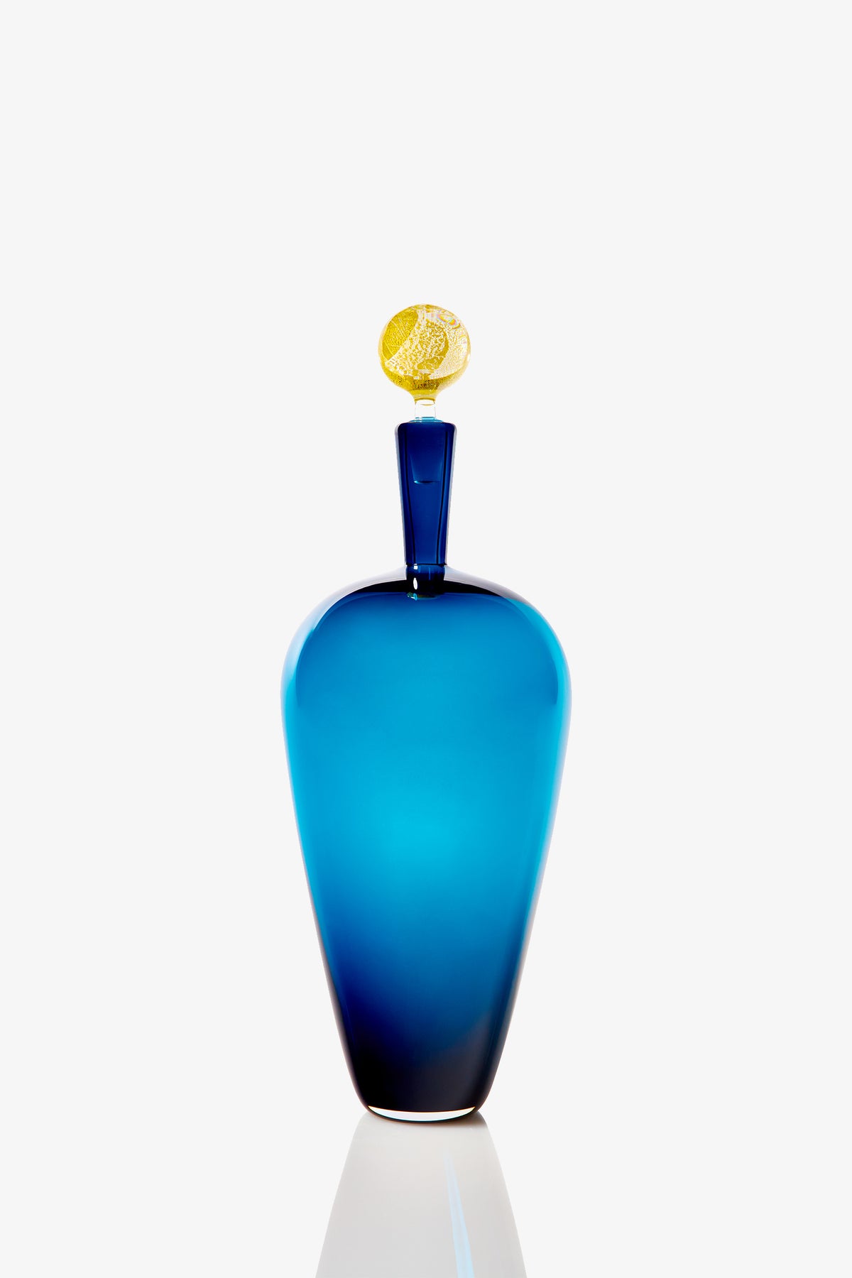 The High Shoulder Carmella Barware is a tall, elegant blue glass vase with a narrow neck and distinctive gold oval stopper, shown against a plain white background.