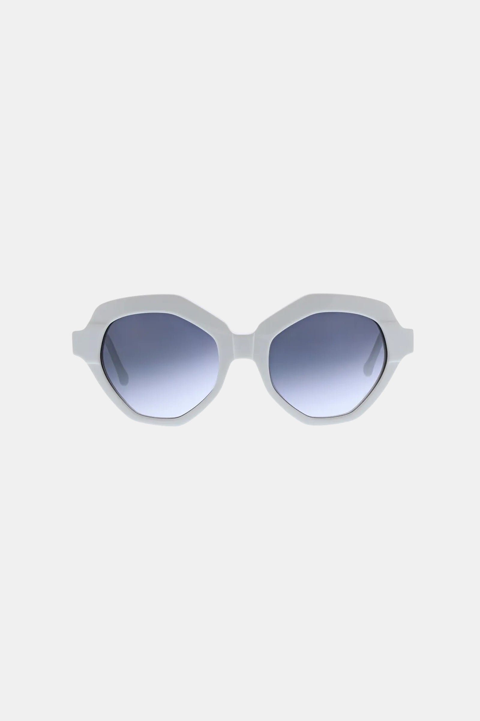 The Ipanema Sunglass features white, geometric-shaped thick frames and blue gradient lenses, showcased against a plain light gray background.