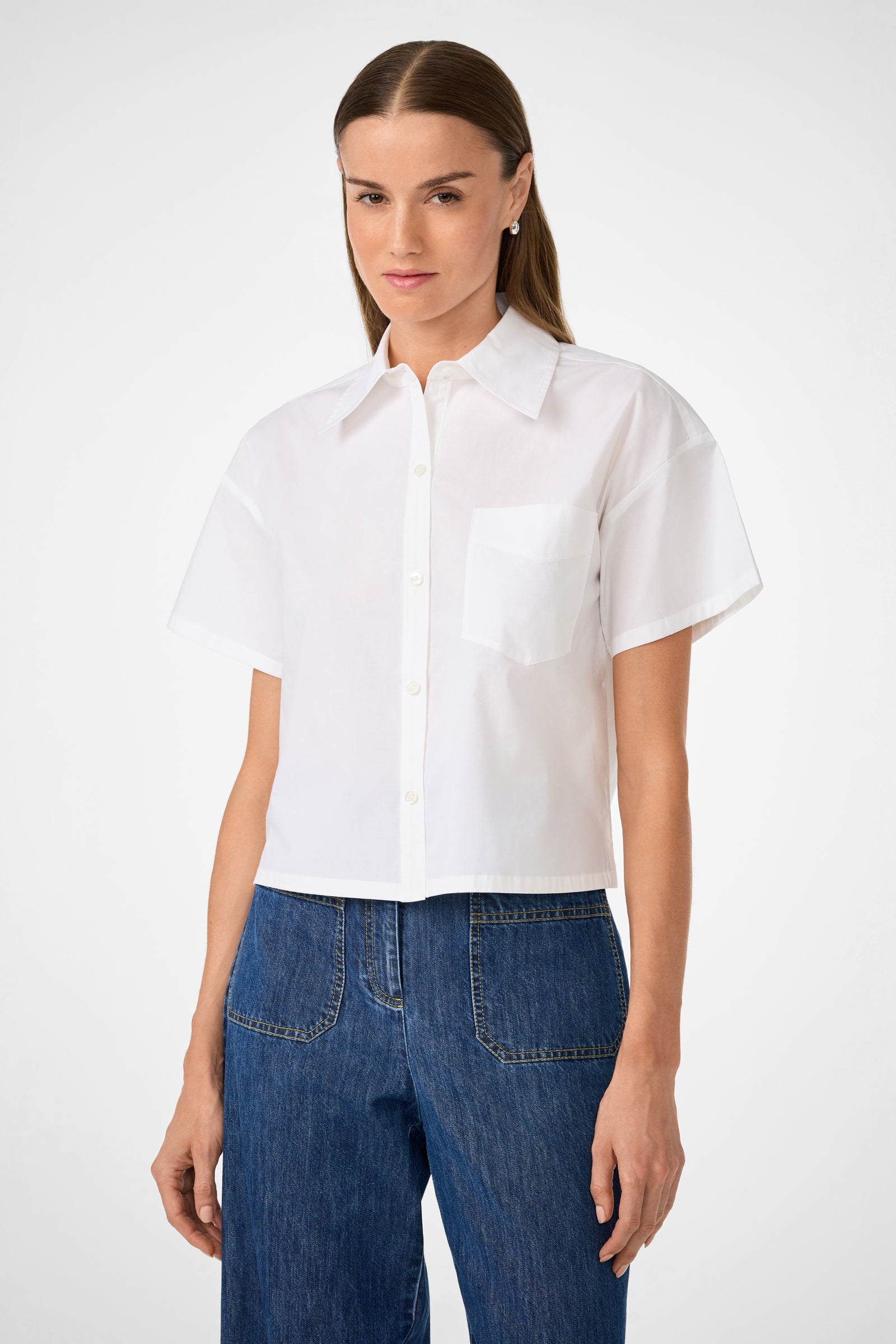 A woman wears the Komore Cropped Button-Front Top in white with blue high-waisted jeans, standing against a plain light background.
