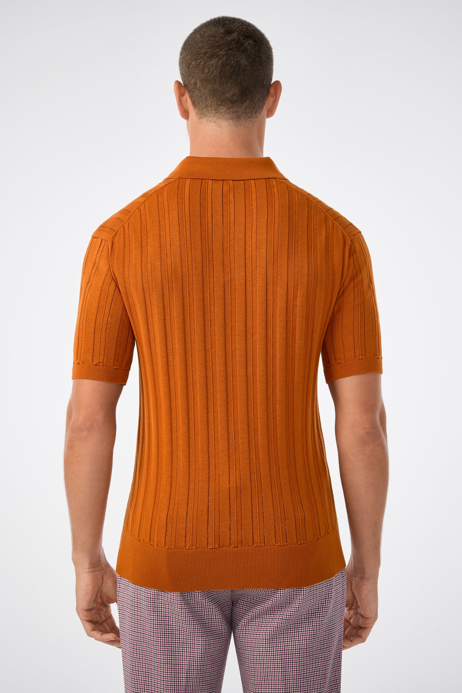A man is seen from behind wearing the Kensington Short-Sleeve Polo in Geranium + Amber and light-colored checkered pants, set against a plain white background.