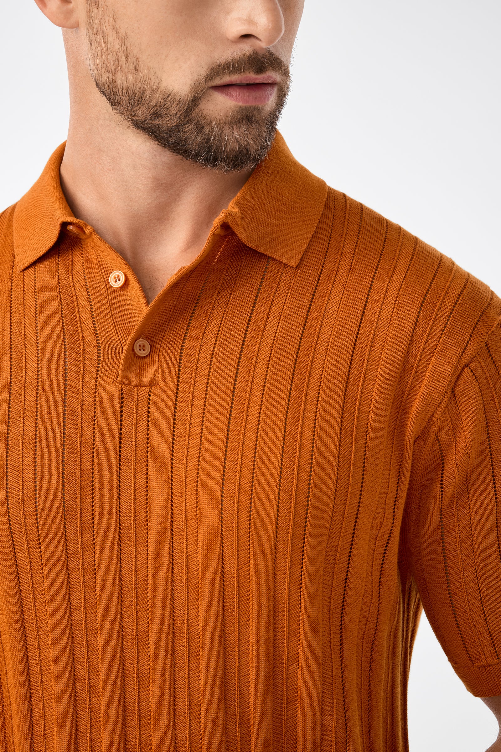 A man with a short beard wears the Kensington Short-Sleeve Polo in Geranium + Amber, shown from the shoulders up, facing slightly sideways against a plain white background.