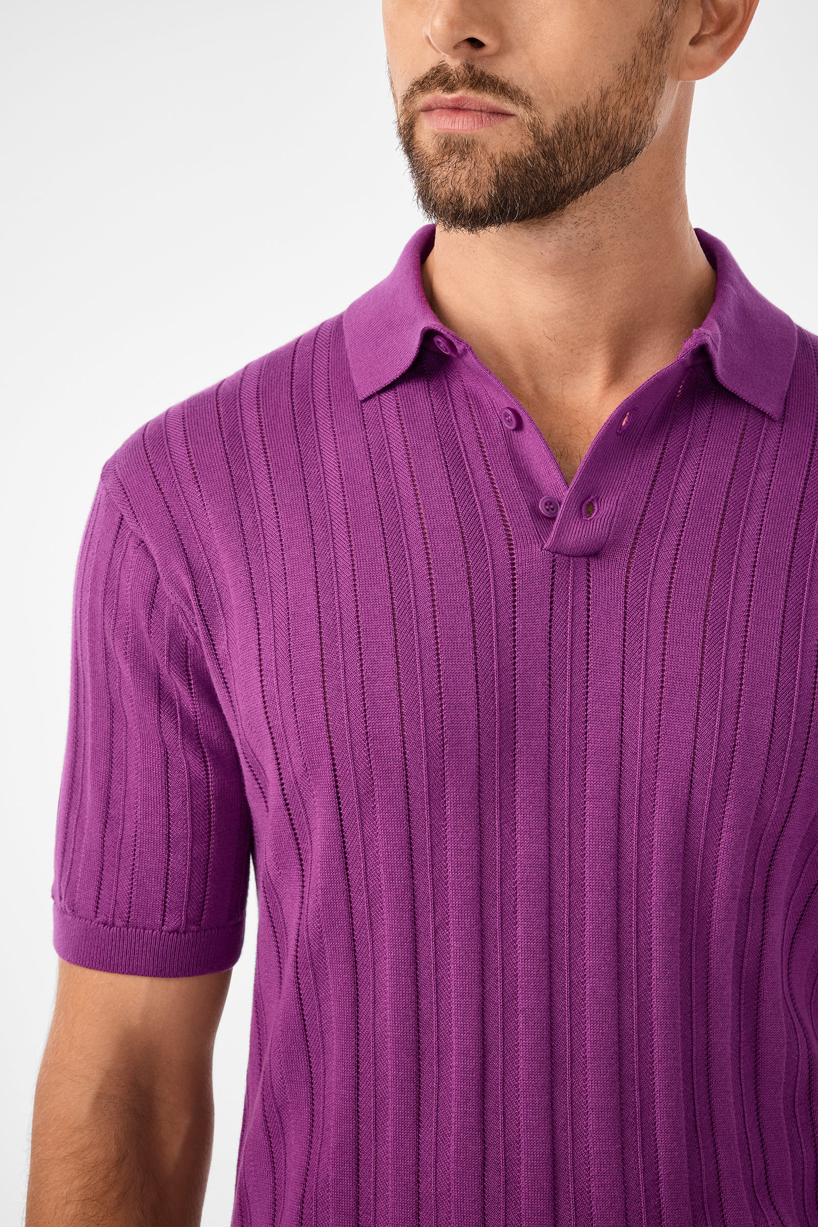 A man with a trimmed beard wears the Kensington Short-Sleeve Polo (Geranium + Amber) with the top two buttons undone. The image captures him from shoulders to mid-chest, set against a plain white background.