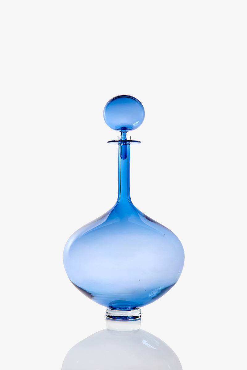 The Large Genie Bottle Decanter, featuring translucent blue glass with a round stopper, wide base, and narrow neck, is displayed against a plain white background.