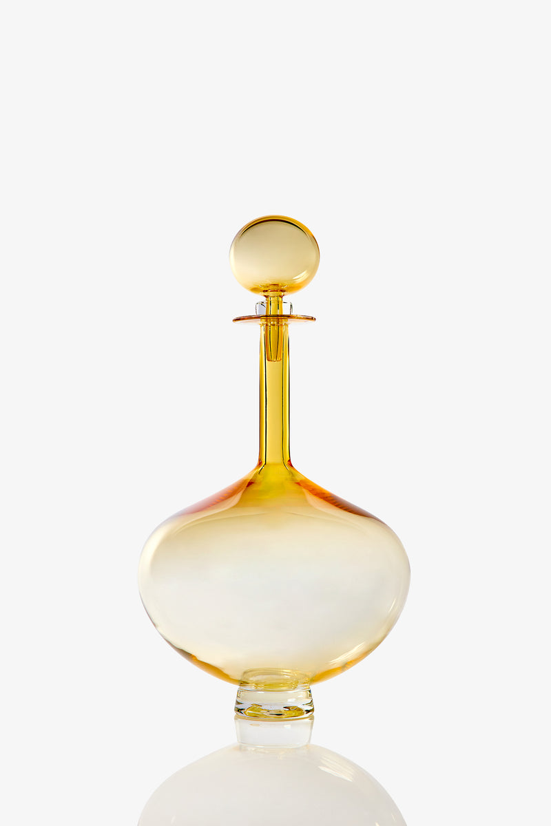 A Large Genie Bottle Decanter, crafted from clear glass with a round stopper and tinted in shades of yellow and orange, is displayed against a white background.