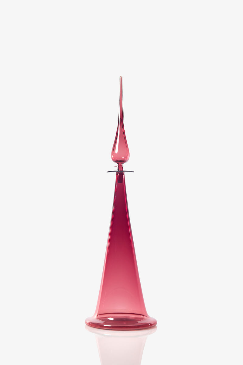 The Large Fluted Cone Decanter features a tall, elegant silhouette crafted from translucent pink glass, with a wide base that gracefully tapers to a sharp, pointed tip. It is showcased against a plain white background.