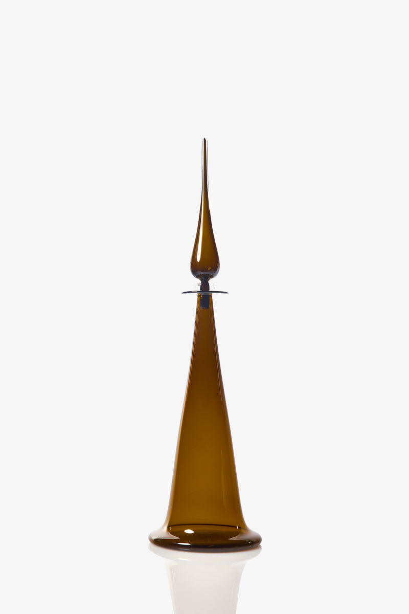 The Large Fluted Cone Decanter is a tall, slender vessel crafted from amber glass, featuring a pointed stopper and resting on a flat base, showcased against a plain white background.