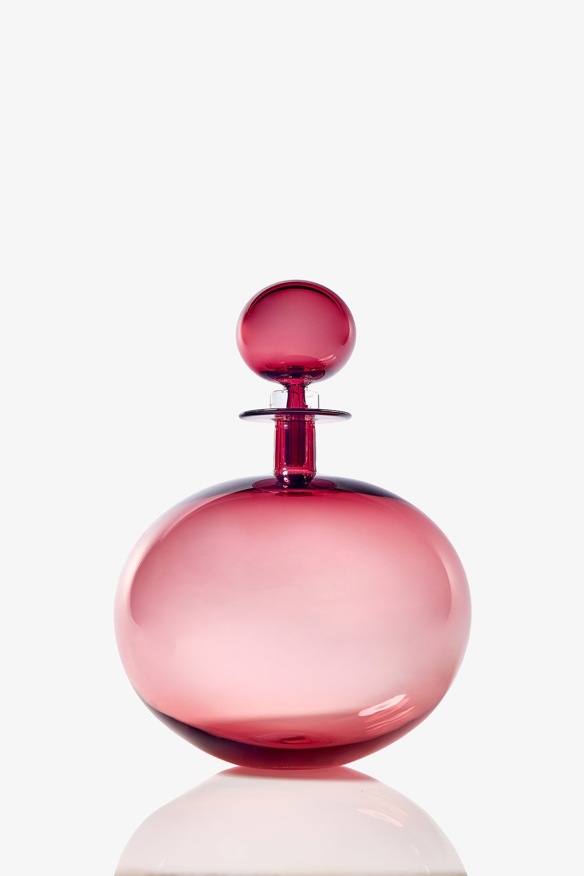 A large, low round decanter made of pink glass with a matching spherical stopper, displayed against a plain white background.