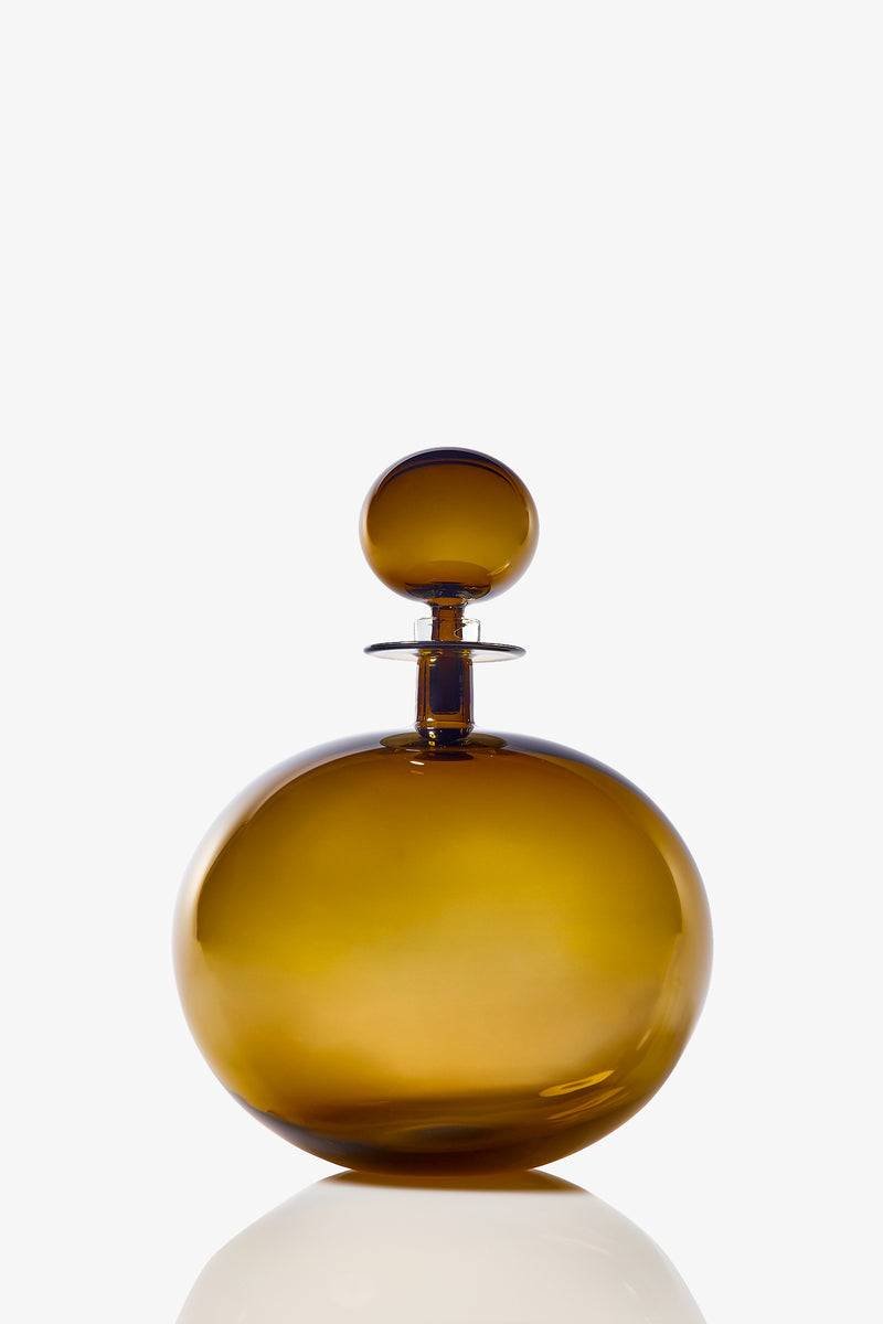 A large, low, round decanter made of amber-colored glass with a matching spherical stopper, set against a plain white background.