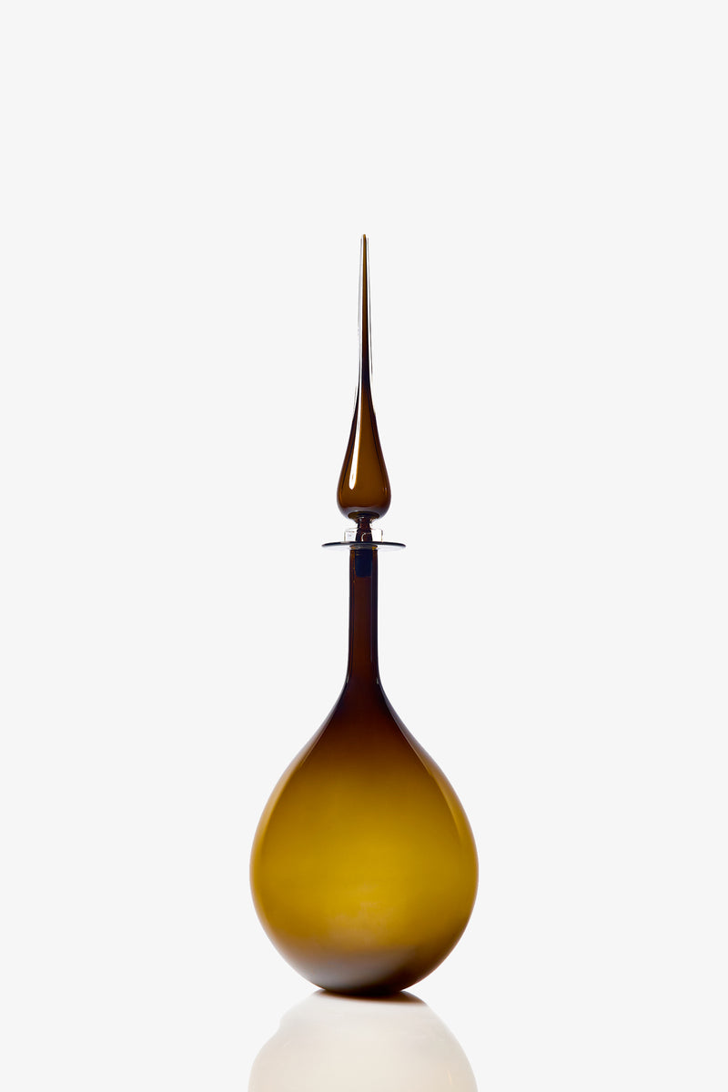 A Large Tear Drop Decanter with a brown glass body and a long, pointed stopper sits on a white background. The decanter features a round base and a tall, slender neck.