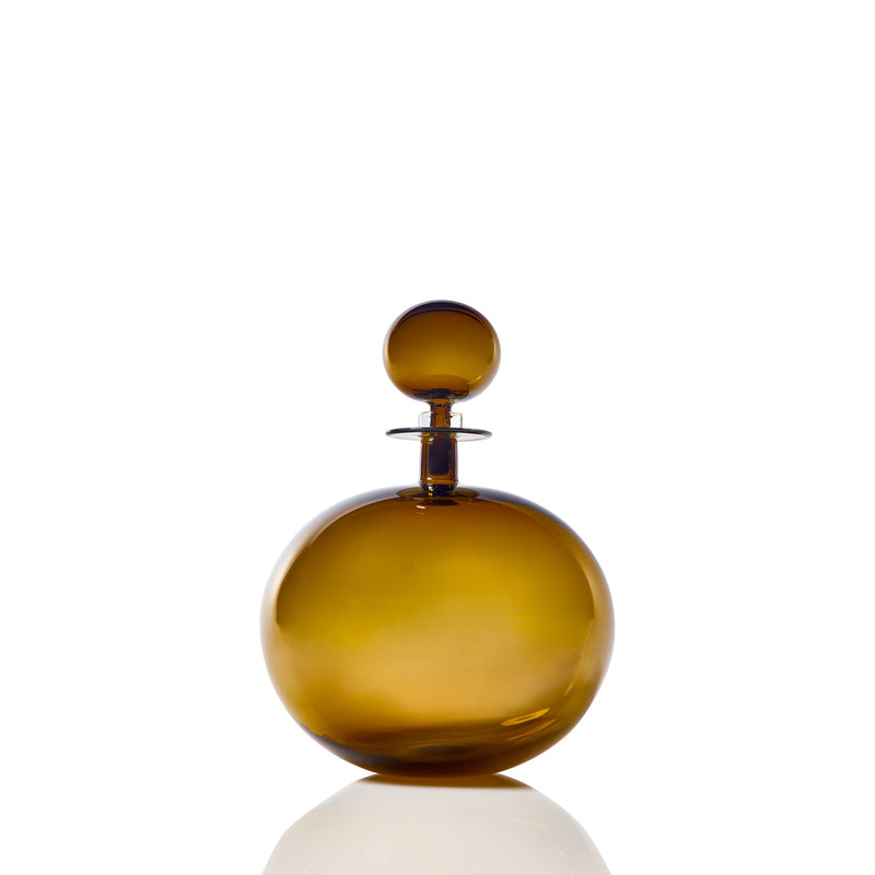 The Petite Low Round Decanter in topaz features an elegant silhouette with a matching spherical stopper, displayed on a white reflective surface against a plain white background.