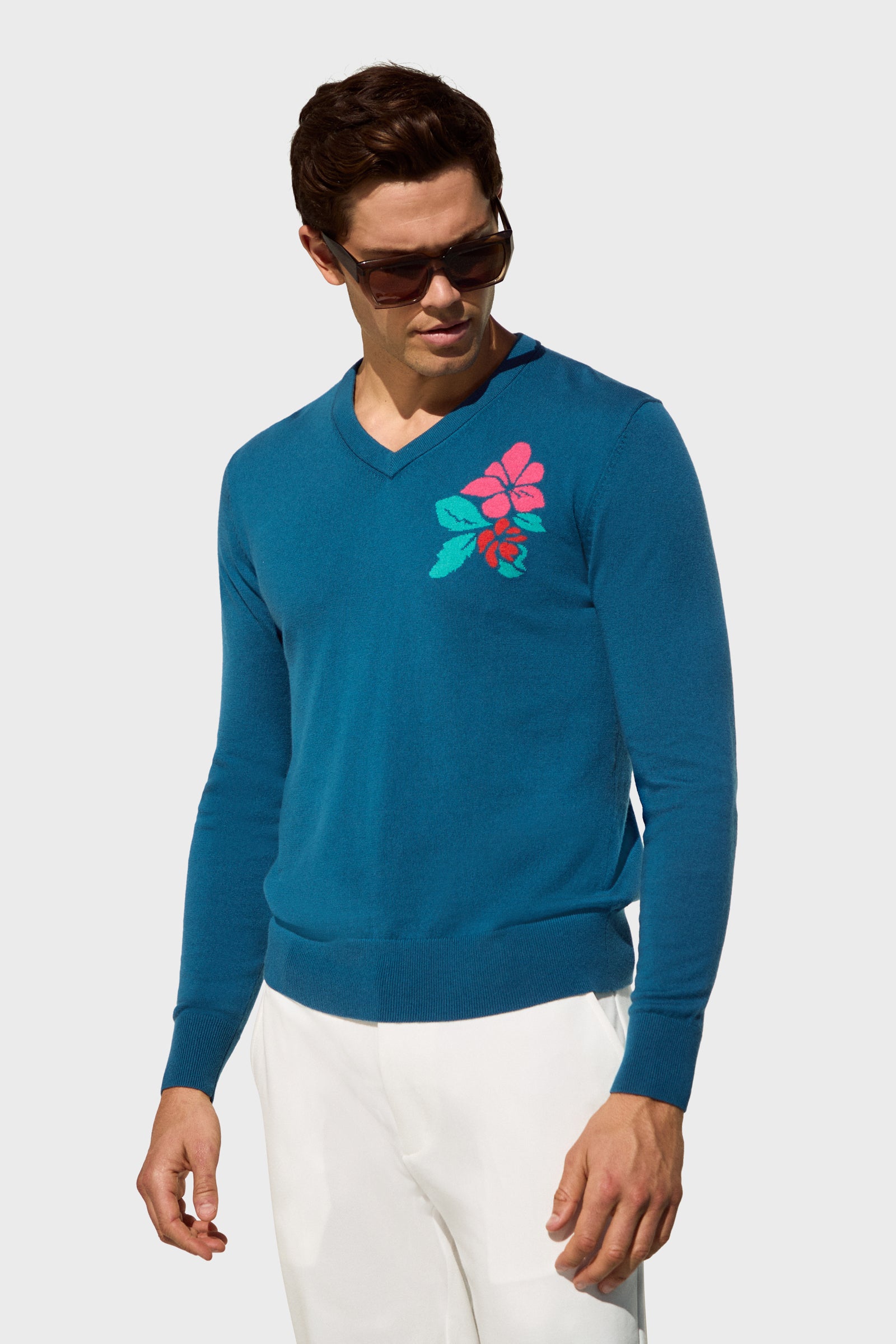 A man wearing sunglasses, white pants, and the Copacabana V-Neck Sweater stands against a plain light gray background.