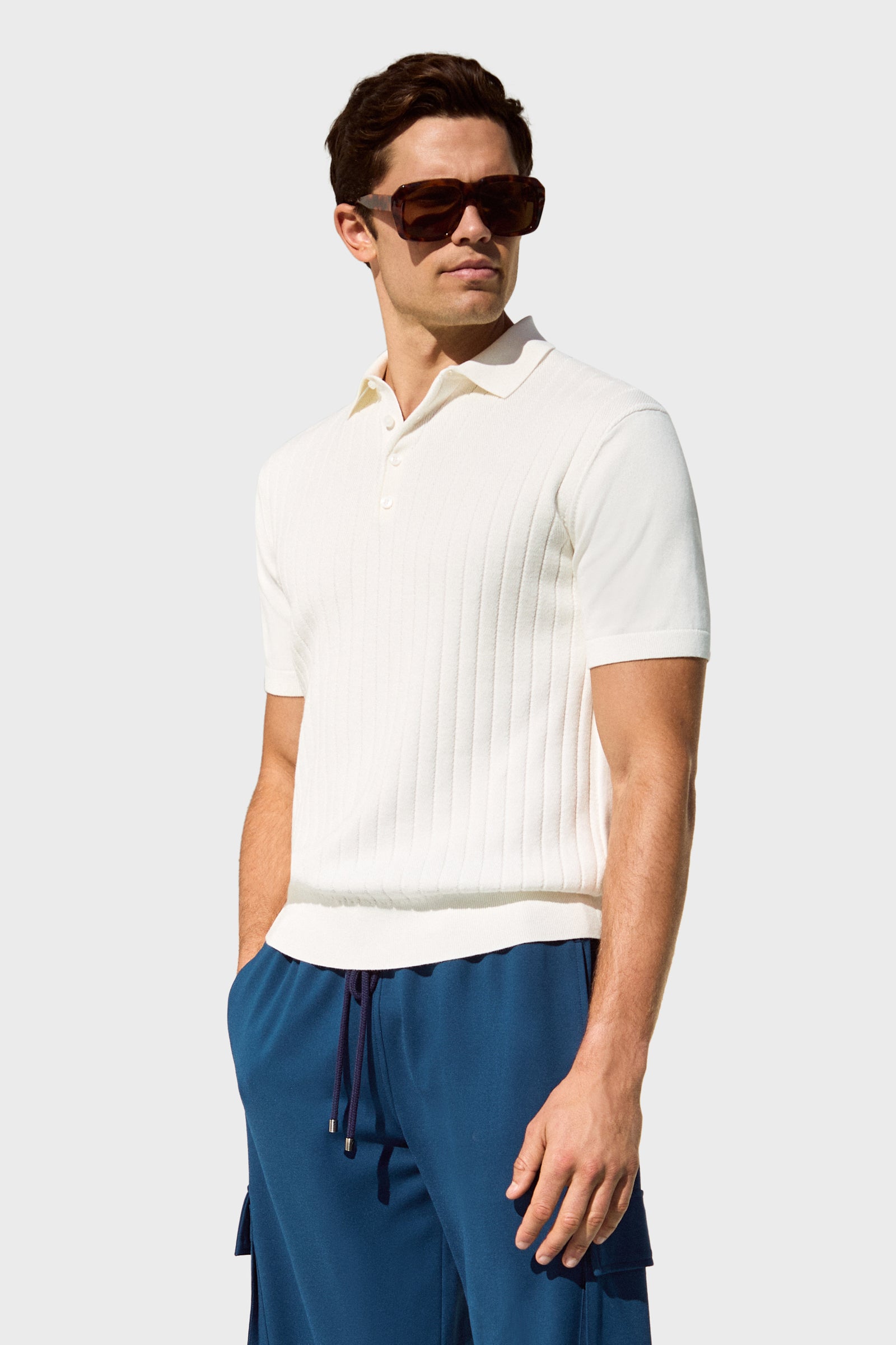 A man in dark sunglasses and the Alvarez Short-Sleeve Polo stands with one hand in his pocket against a light gray background.