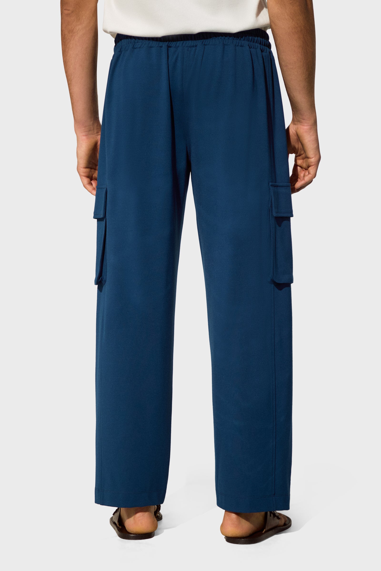 A person is shown from the waist down wearing the Lounge Cargo Pant in navy blue with side pockets and sandals, standing against a plain light background.