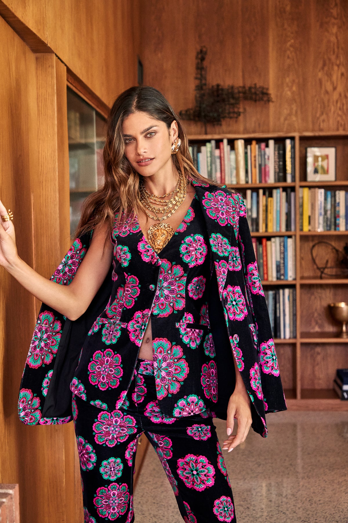 A person wearing a Raylee Top black blazer and matching trousers featuring a vibrant pink and teal floral pattern, accessorized with layered gold chain necklaces.