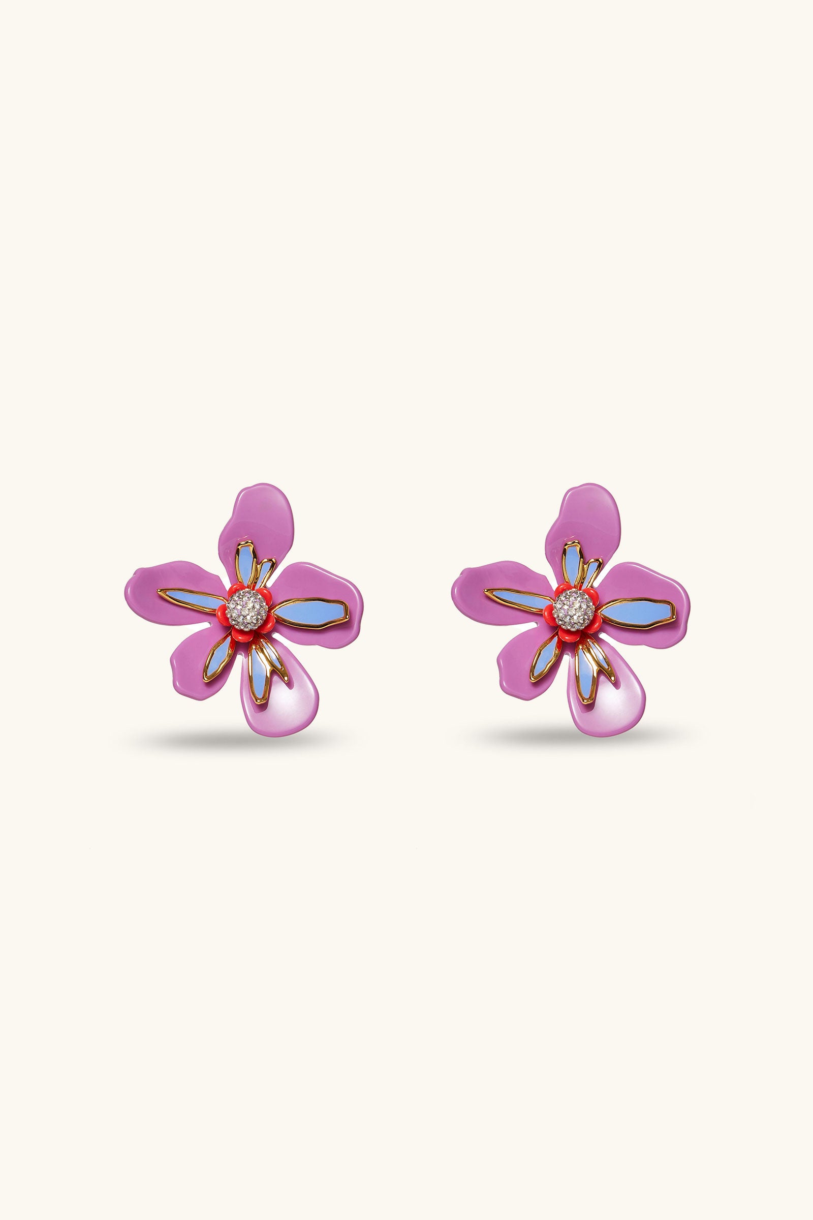 The Lele Sadoughi x Trina Turk Soie Paradis Earrings are magenta, flower-shaped with gold outlines and orange centers, shown against a light beige background.
