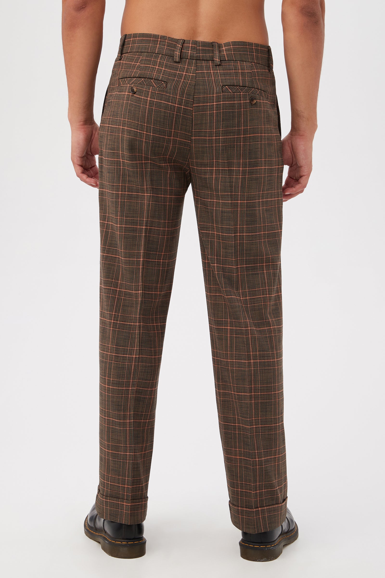 A person faces away from the camera, wearing Genet Wide-Leg Trousers in Chaka Check Plaid and black shoes. Their upper body is bare, set against a plain white background.