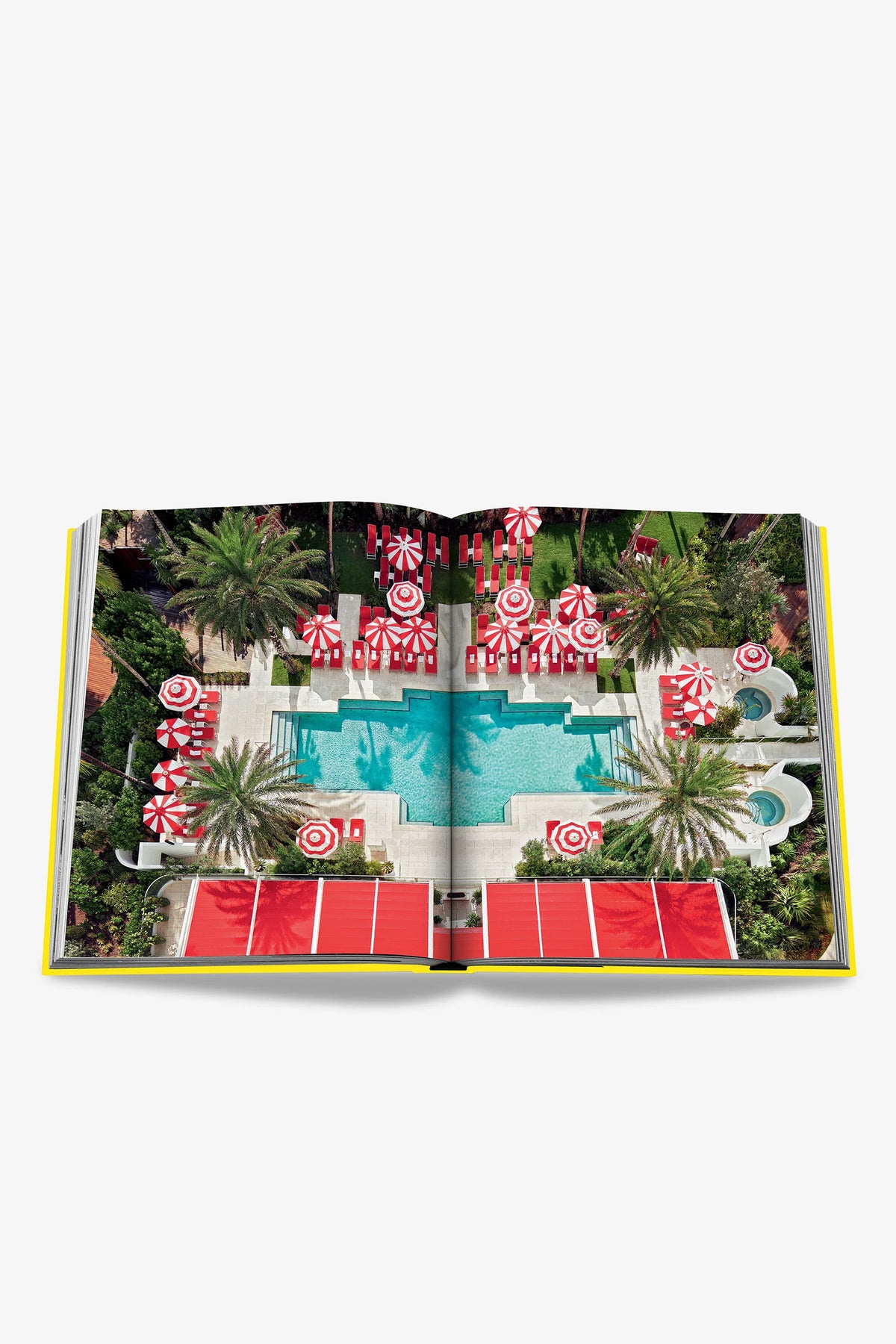 An open Assouline Miami Beach Book displaying a photo of a pool surrounded by palm trees and red-and-white striped umbrellas, viewed from above.
