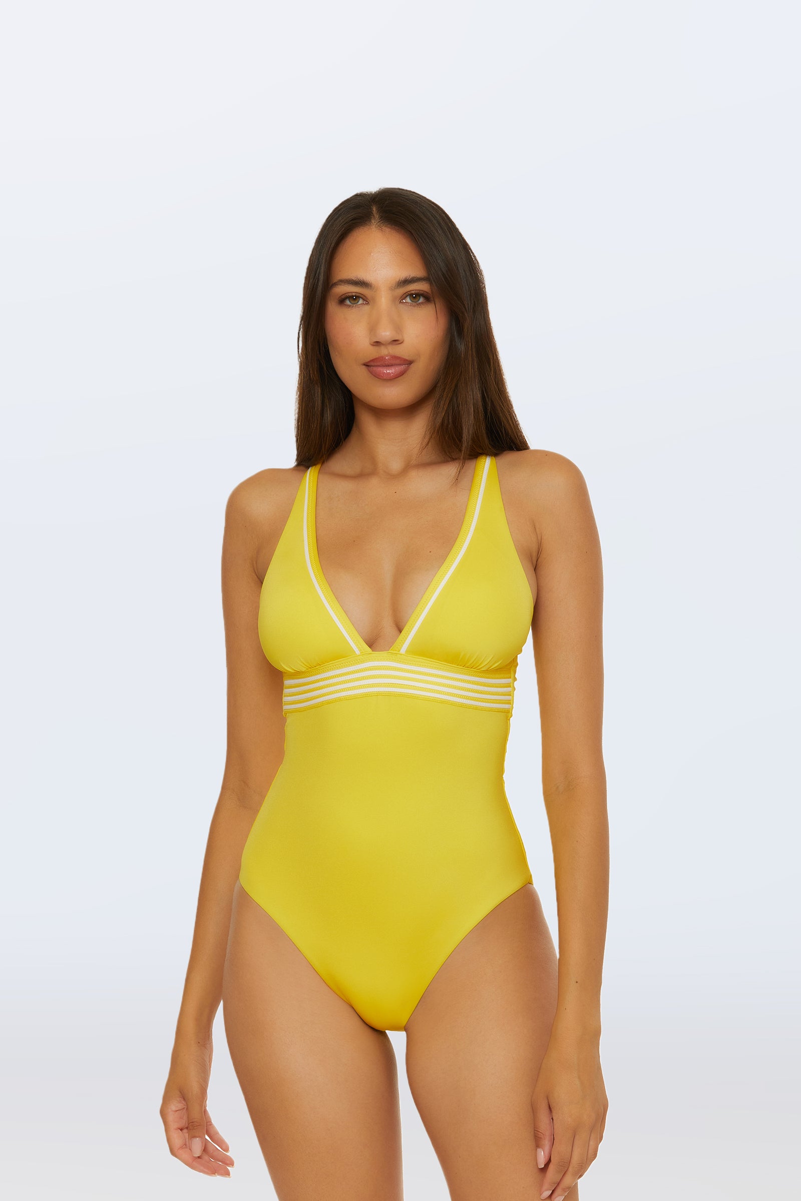 A woman with long brown hair faces forward against a plain light background, wearing the Monaco Pleated Plunge One-Piece swimsuit in Desert Sun.