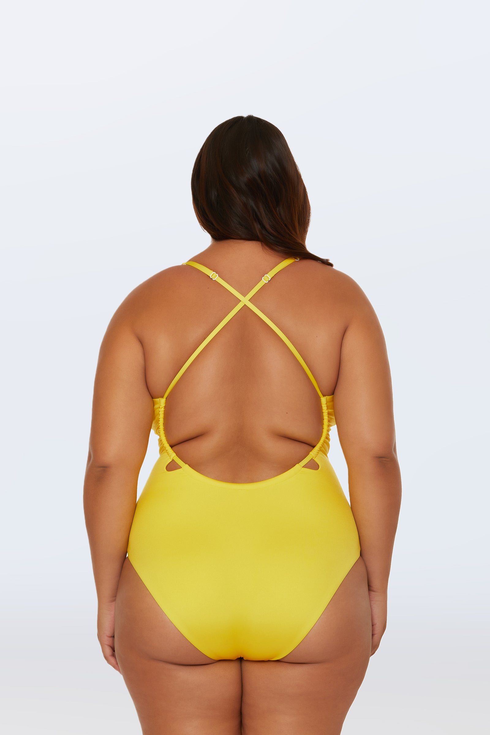 A woman is seen from the back in the Monaco Pleated Plunge One-Piece, a bright yellow swimsuit with crisscross straps and an open back, set against a plain light background.