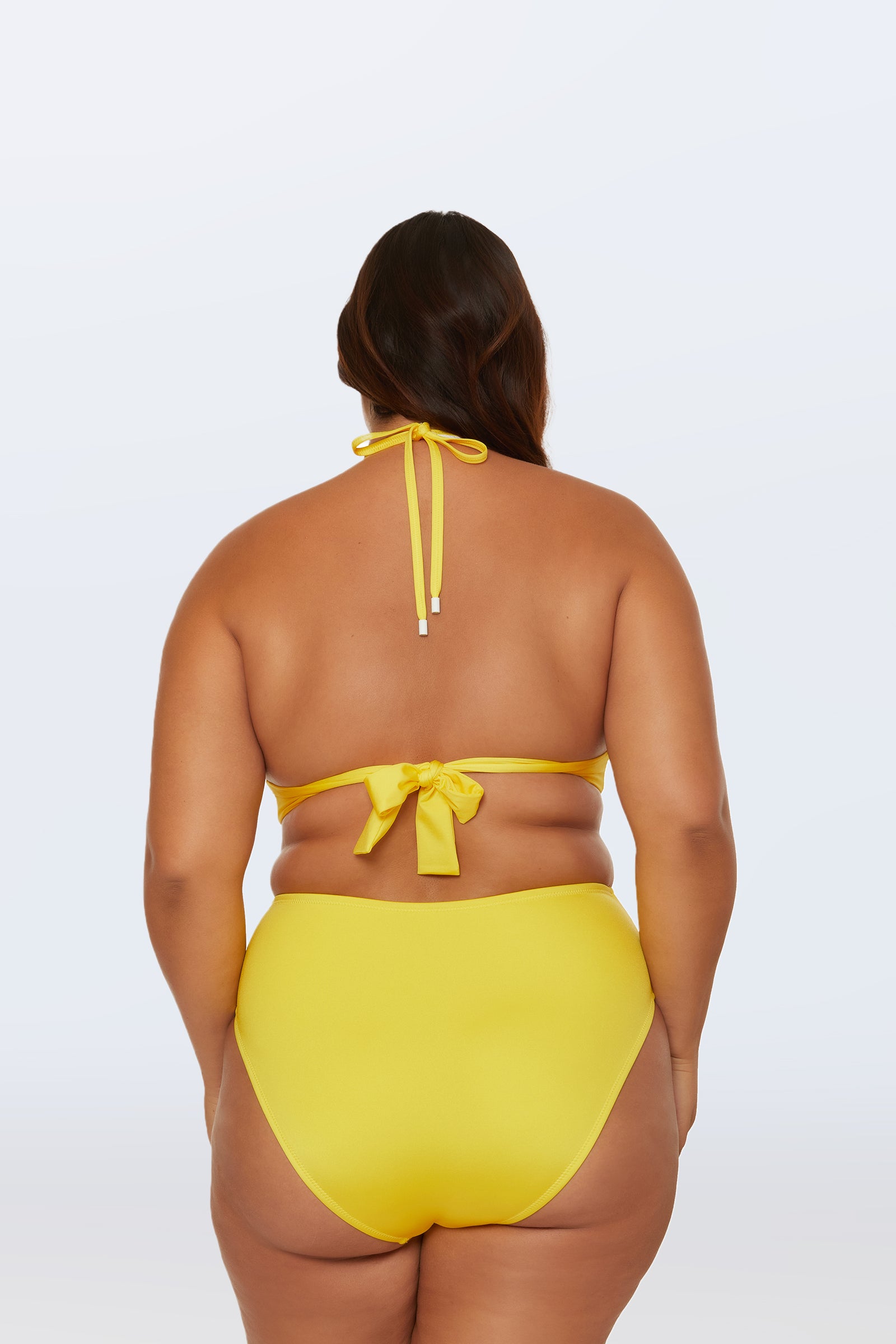 A woman with long brown hair is shown from behind wearing the Monaco Pleated Halter Triangle Top in bright yellow, tied at the neck and back, standing against a plain light background.