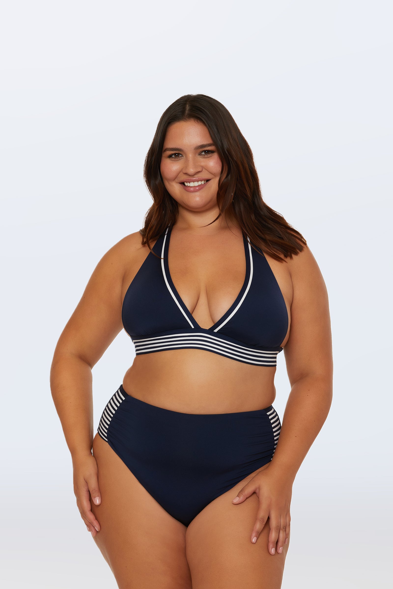 A woman with long brown hair smiles while wearing the Monaco Pleated High-Waist Bikini Bottom in navy blue with white and navy striped trim, set against a plain white background.