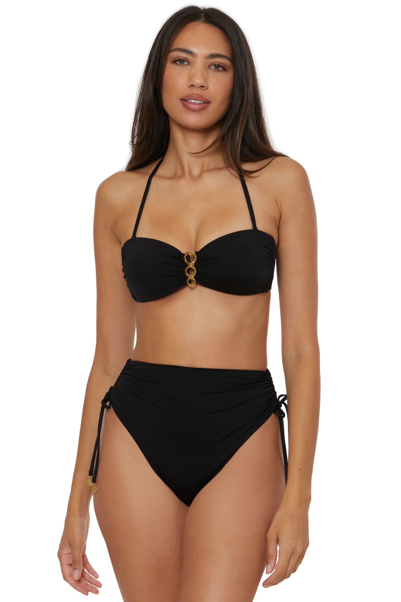 A woman wears the Monaco Shirred Tie High-Waist Swim Bottom—a black bikini with gold ring accents and side-tie, high-waisted bottoms—standing against a plain white background.