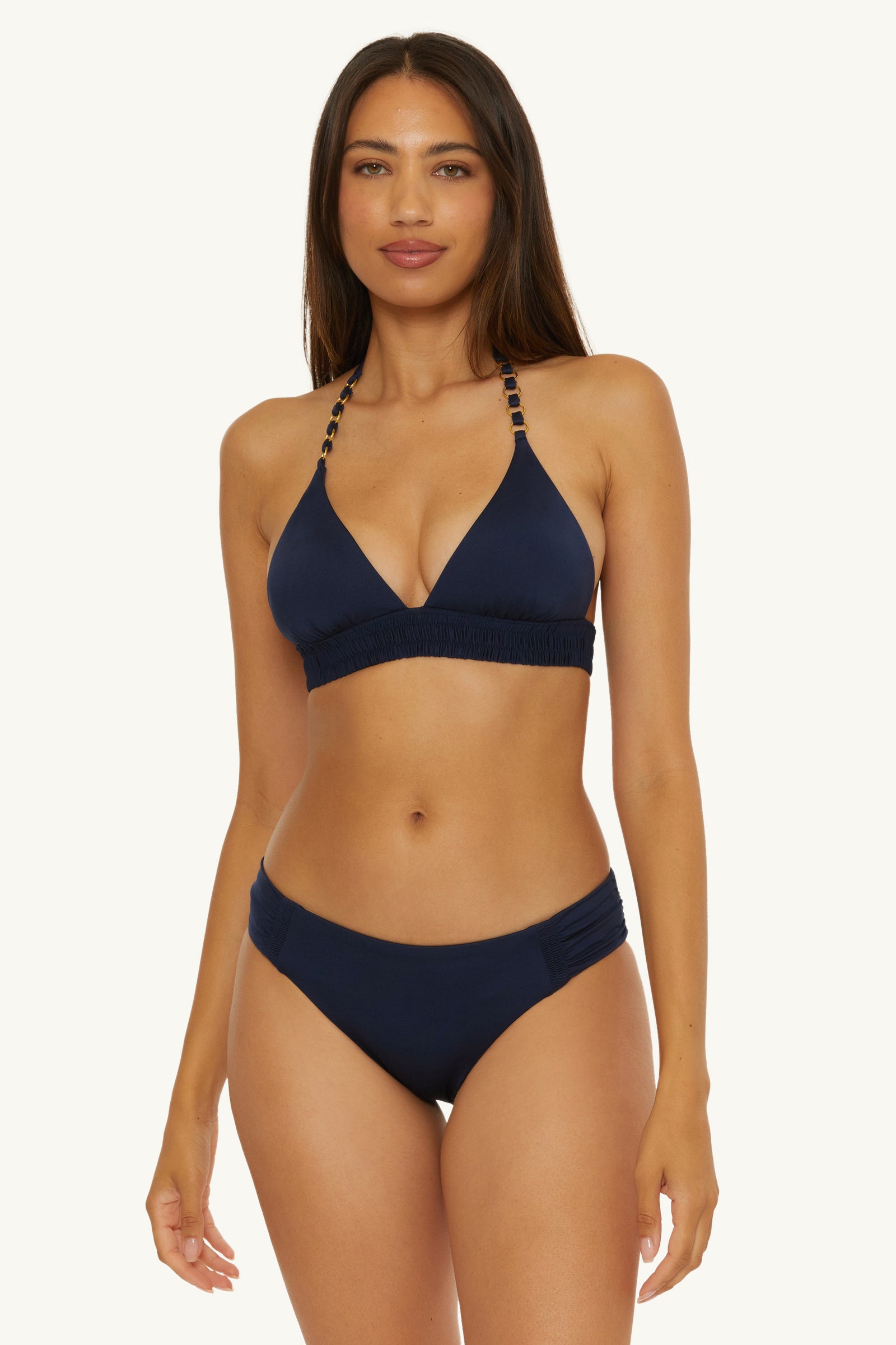 A woman with long brown hair wears the Ring Halter Swim Top - Monaco, a dark blue bikini with beaded straps and matching bottoms, standing against a plain light background.