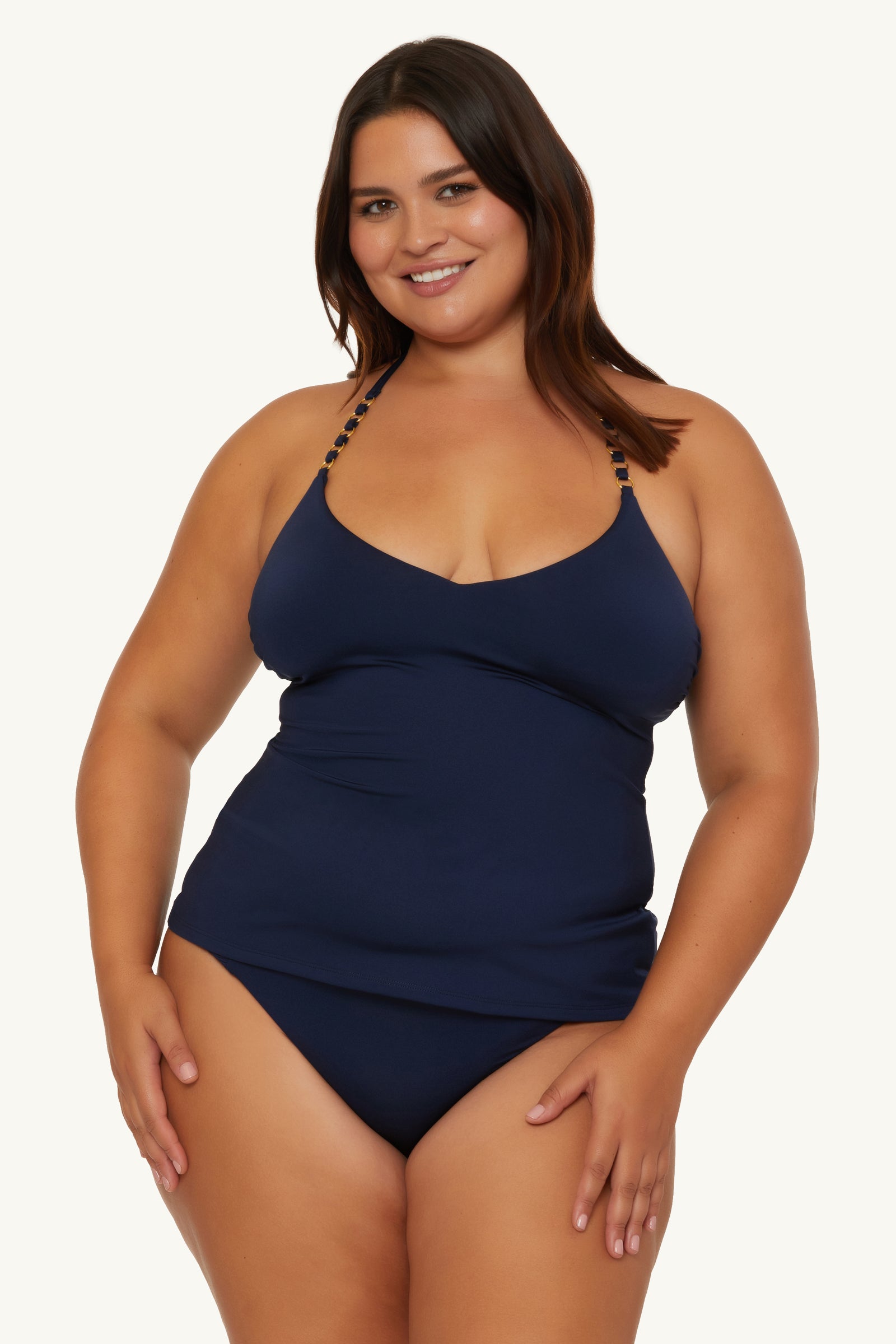 A woman with long dark hair smiles while wearing the Ring Tankini Swim Top - Monaco, a navy blue halter-neck swimsuit, against a plain light background.