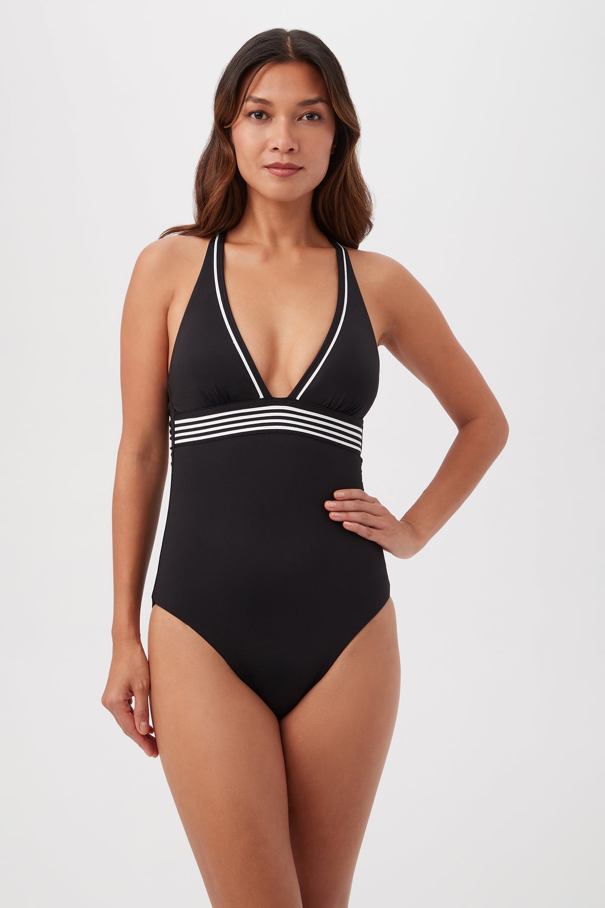 A woman models the Monaco Pleated Plunge One-Piece in Black/White, featuring a deep V neckline and white striped detailing under the bust, against a plain background.