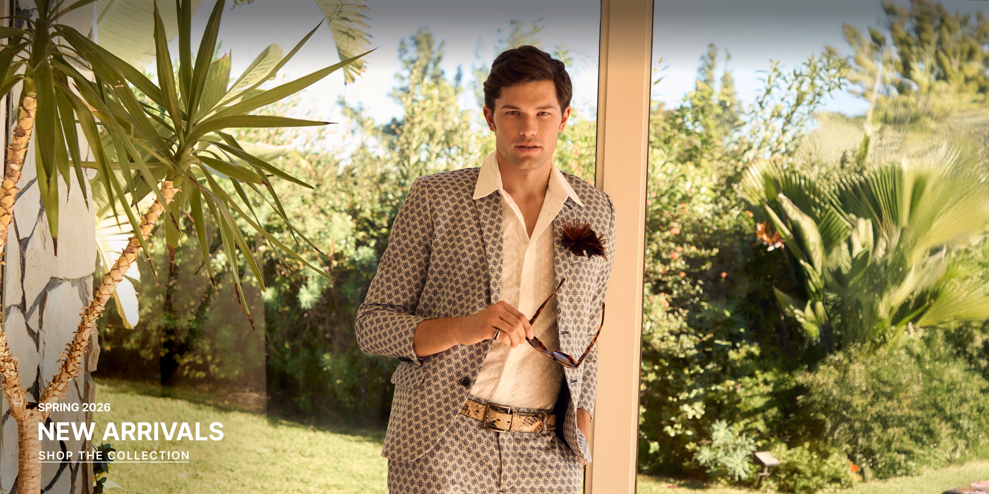 Man in a patterned suit standing in a garden with palm trees.