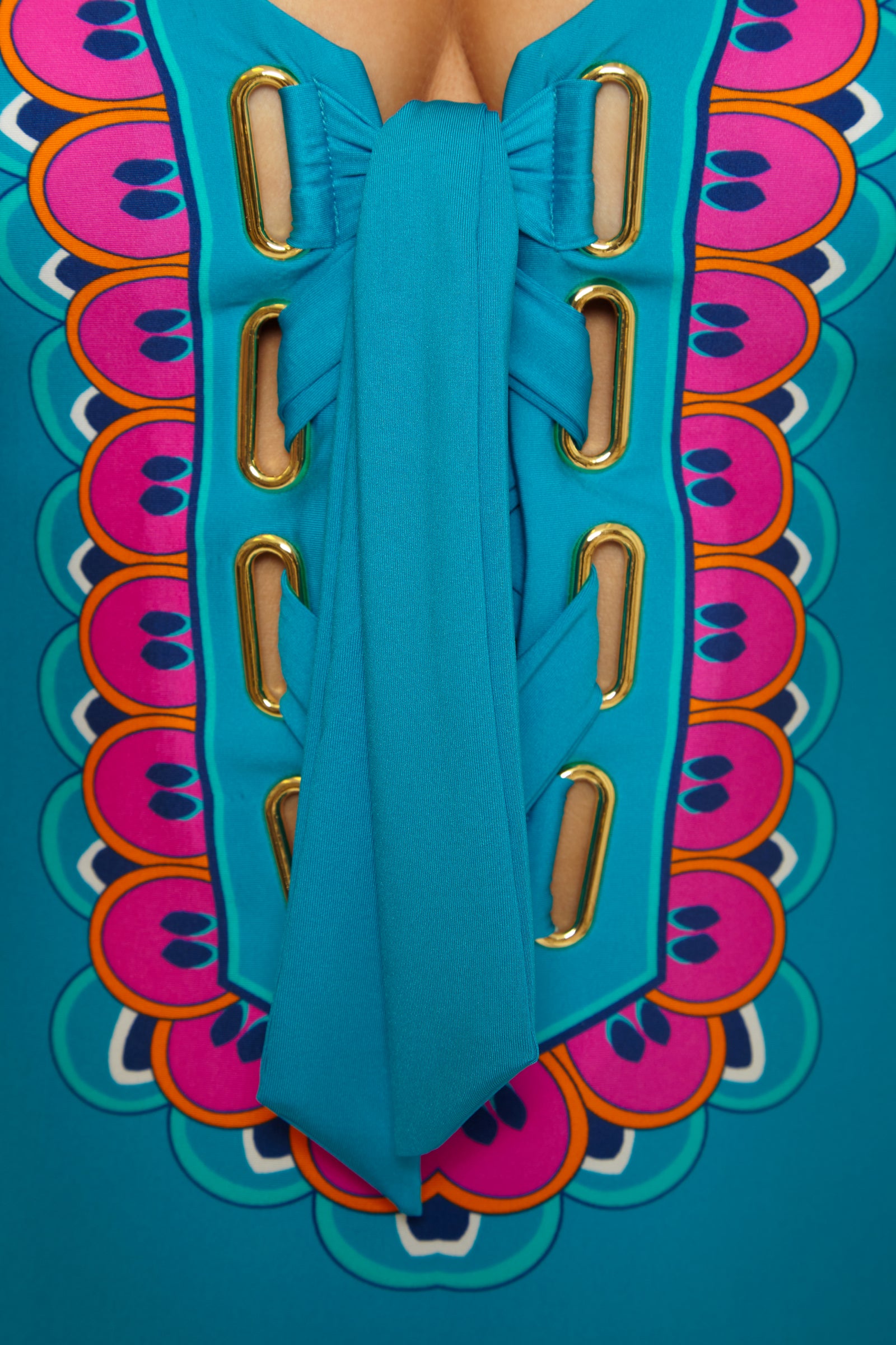 Close-up of the Mykonos Lace Up Maillot: a vibrant turquoise swimsuit with gold eyelets, wide blue lacing, and a colorful scalloped pattern in pink, orange, and purple around the lace-up front.