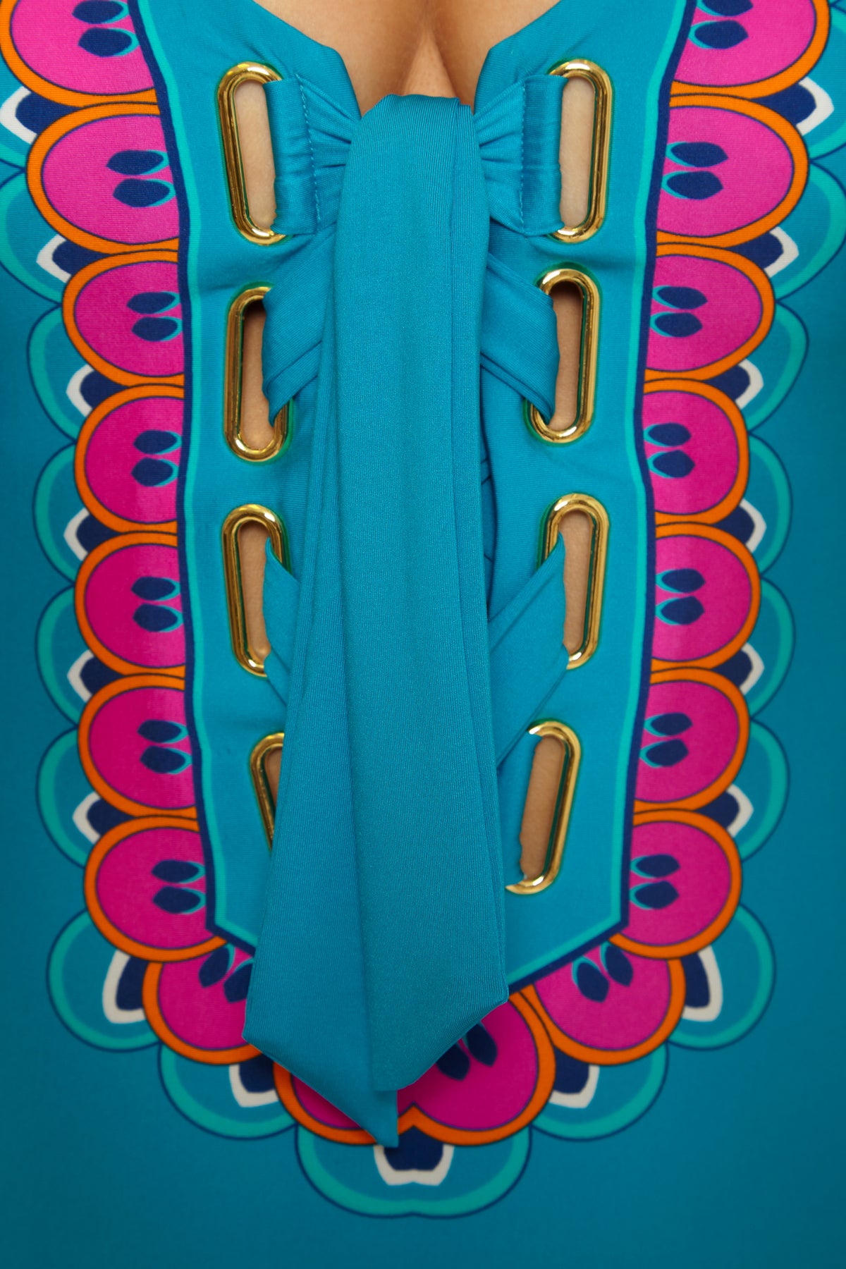Close-up of the Mykonos Lace Up Maillot: a vibrant turquoise swimsuit with gold eyelets, wide blue lacing, and a colorful scalloped pattern in pink, orange, and purple around the lace-up front.