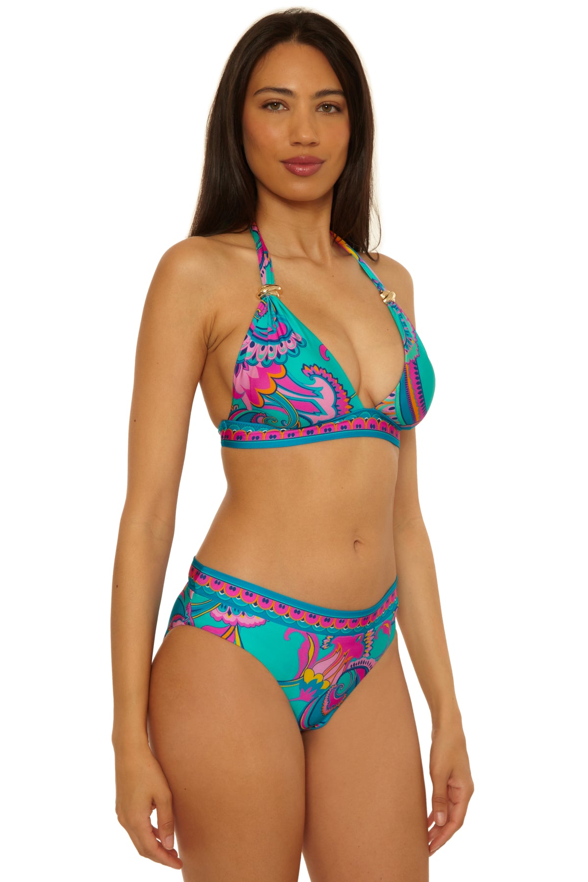 A woman with long brown hair models the Mykonos Reversible Hipster, a turquoise bikini featuring a colorful, paisley-inspired pattern. She stands facing the camera against a white background.