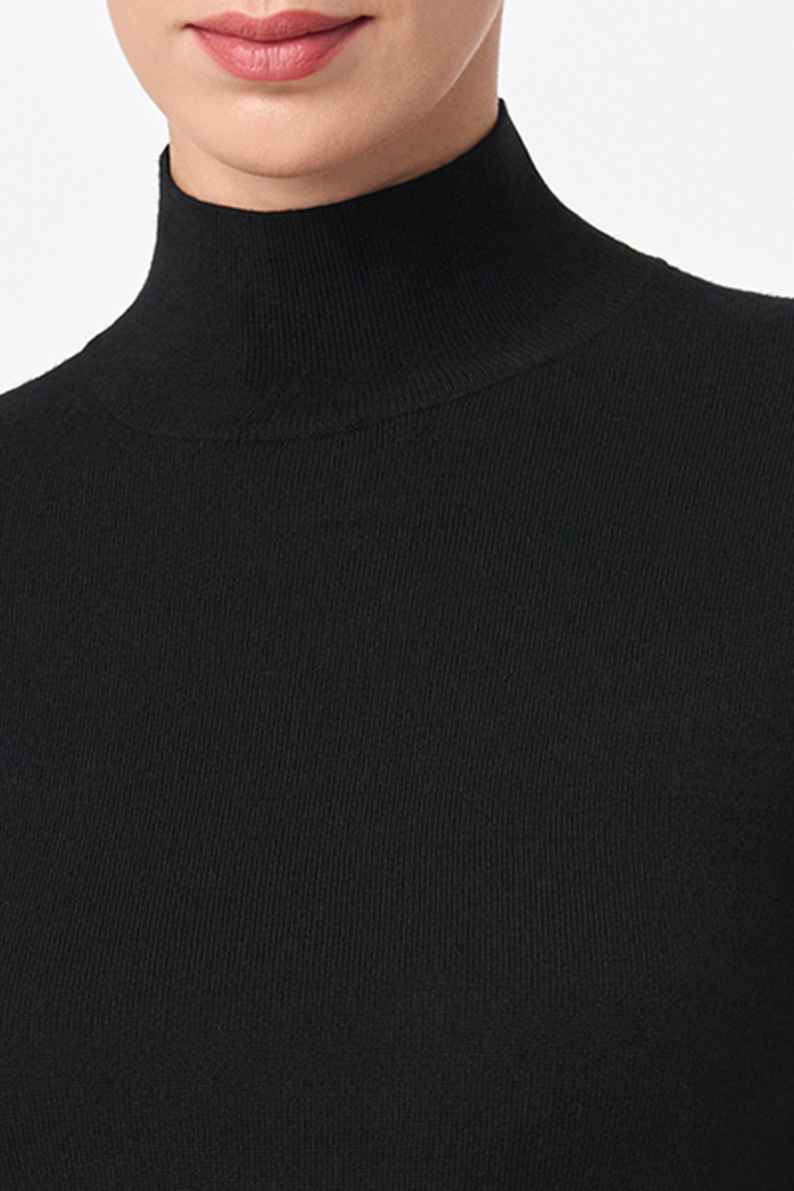 A close-up of a person wearing the Mali Mock Neck black ribbed sweater against a plain white background, showing only the lower half of the face and neck.