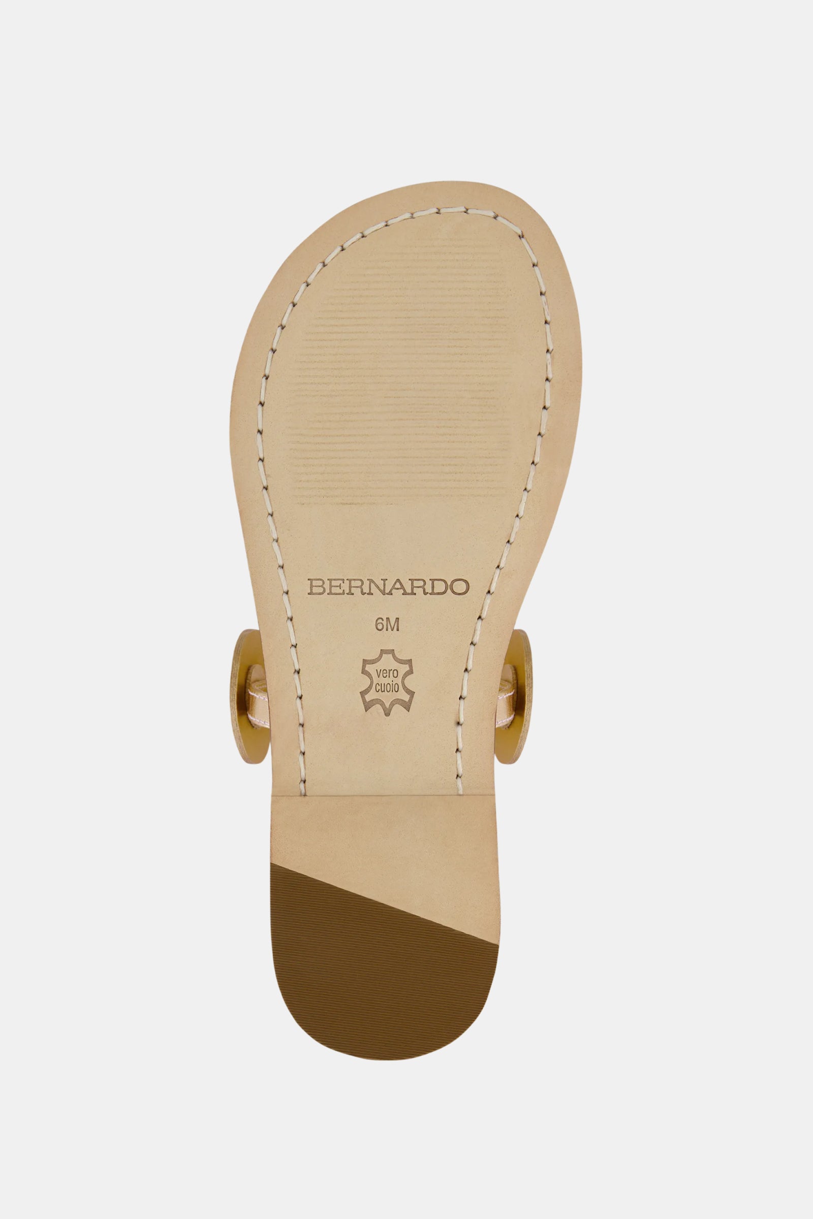 The underside of the Bernardo New Moon Sandal in beige features light stitching, BERNARDO branding, and a star-shaped leather stamp on the sole. Gold circular hardware accents are visible on the sides.