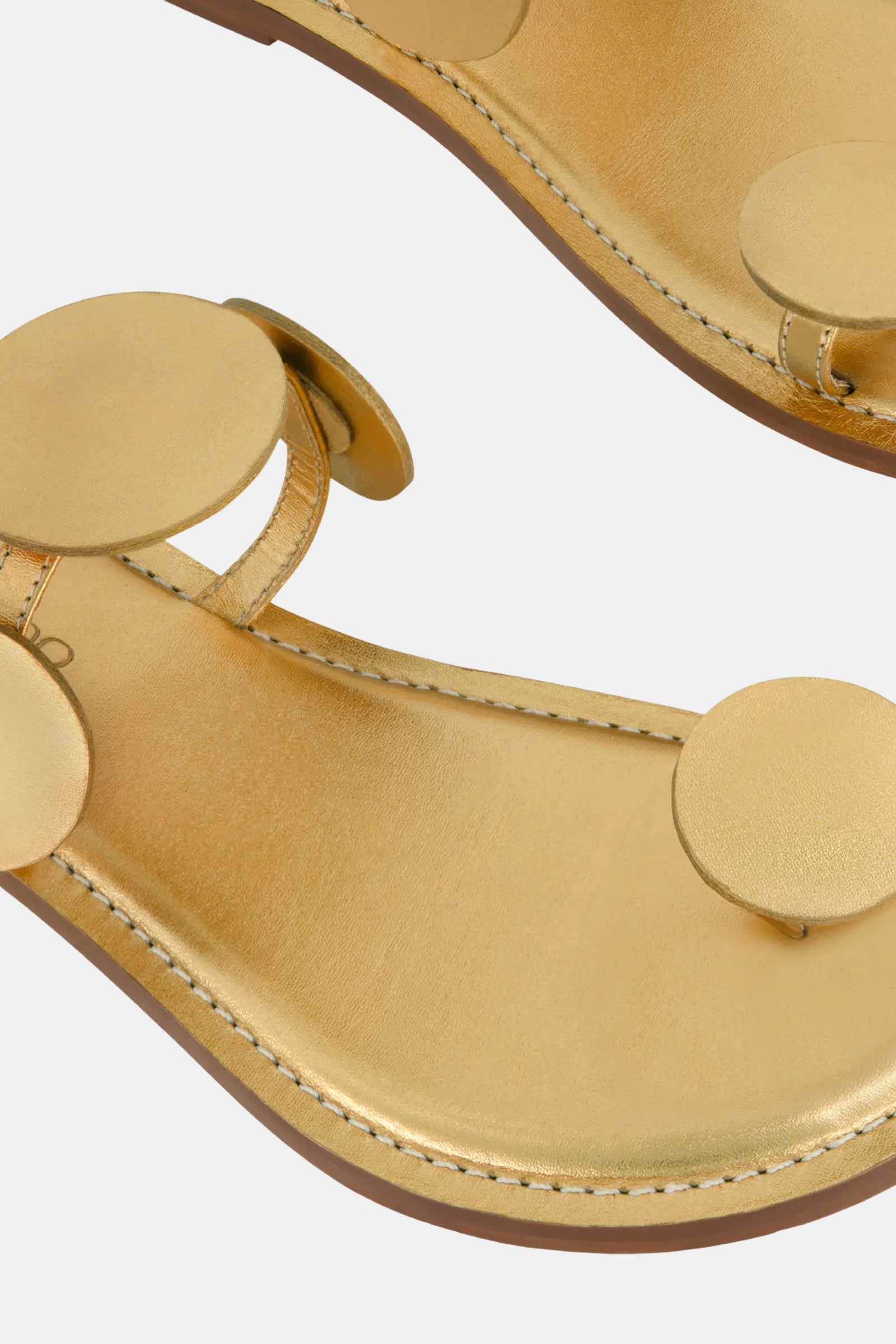 Close-up of the Bernardo New Moon Sandal, showcasing large circular gold accents on the strap and footbed, visible stitching on the edges, and a light brown sole.