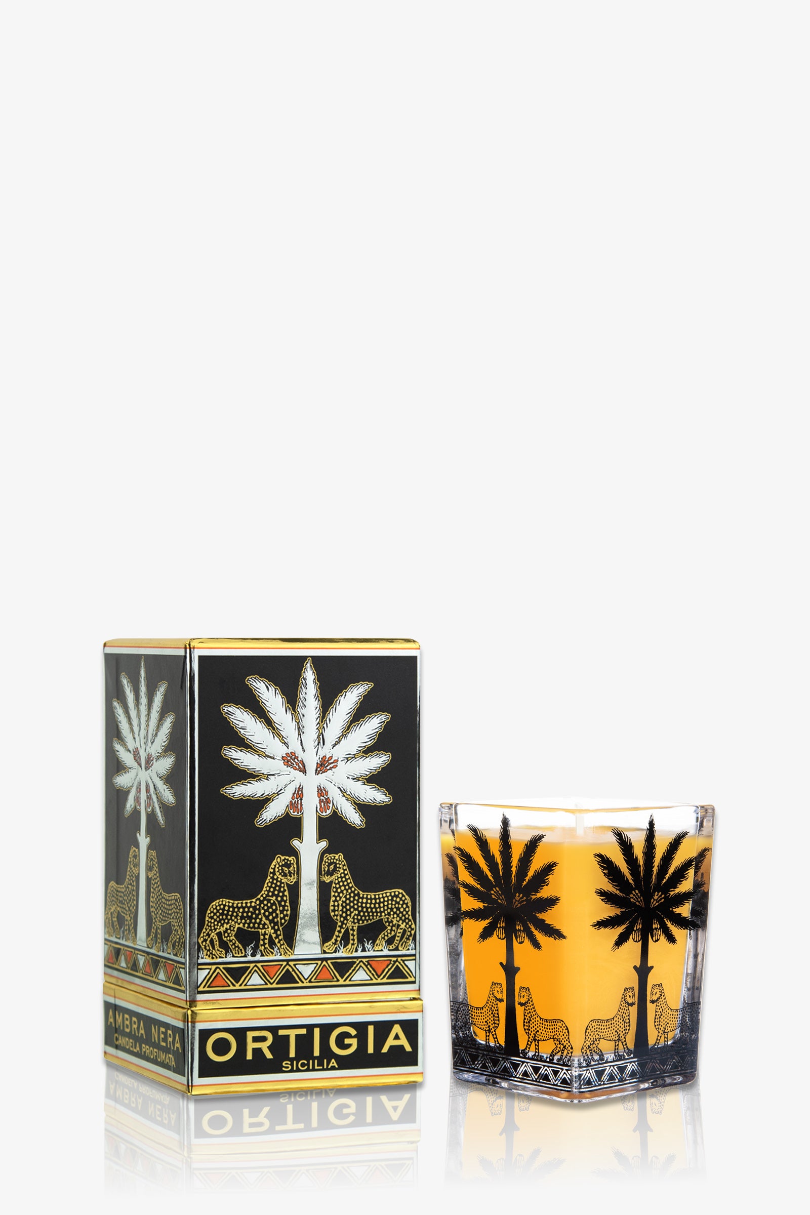 The Ortigia Ambra Nera Candle Large Square in amber sits next to its matching box, both adorned with gold and black palm tree and leopard designs.