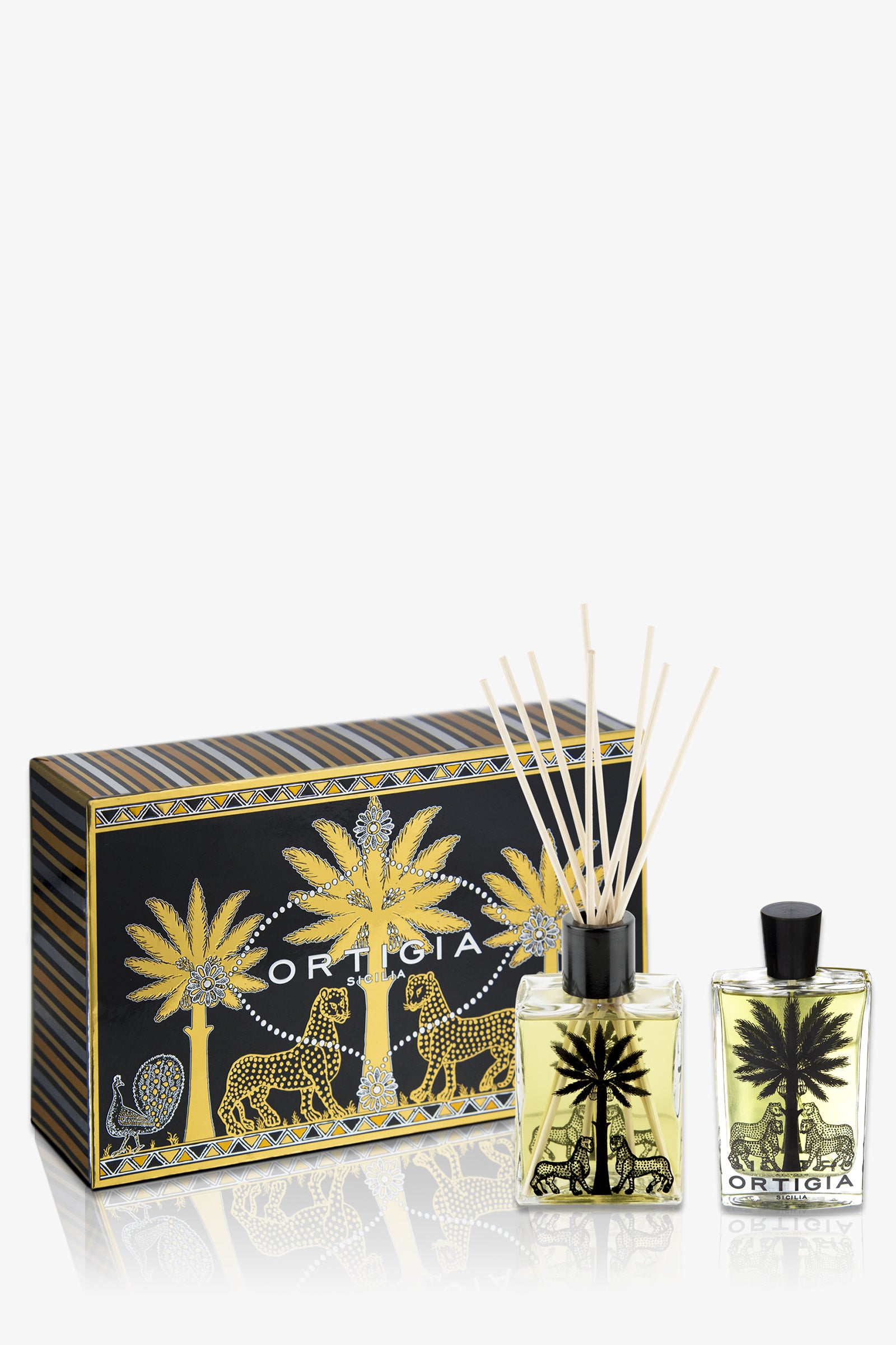The Ortigia Ambra Nera Casa Set features a decorative amber-colored perfume and diffuser in a black and gold box adorned with palm tree and leopard designs, with both bottles showcasing matching motifs.