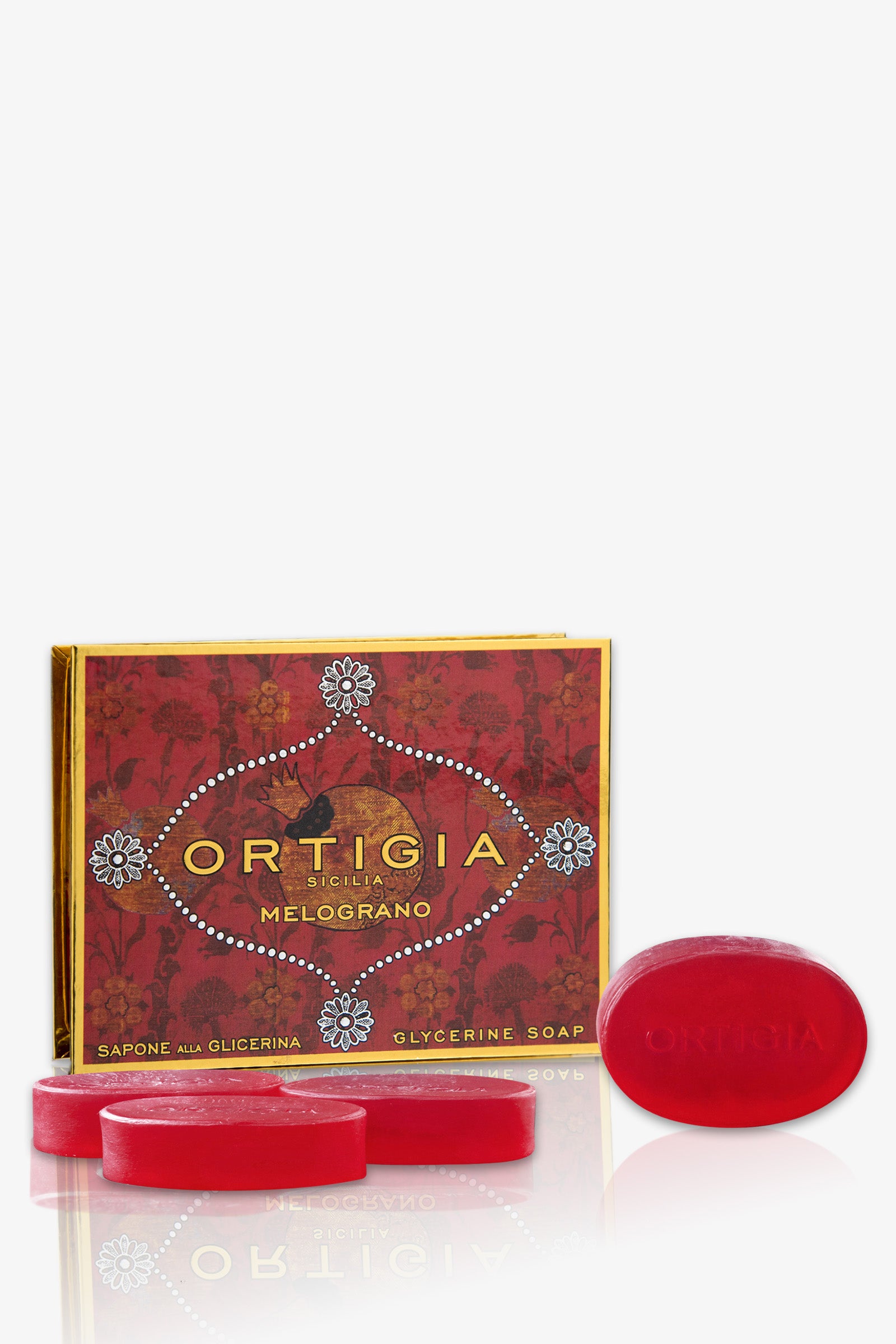 The Ortigia Melograno Soap Set features oval red glycerine bars and a decorative red and gold box with floral designs and white accents. One soap is upright, displaying the Ortigia name.