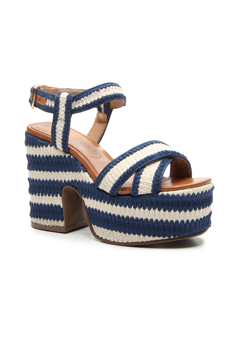 The Zamzibar Platform is a blue and white striped sandal with crisscross straps, an open toe, ankle strap, chunky heel, woven texture, and a buckle closure.