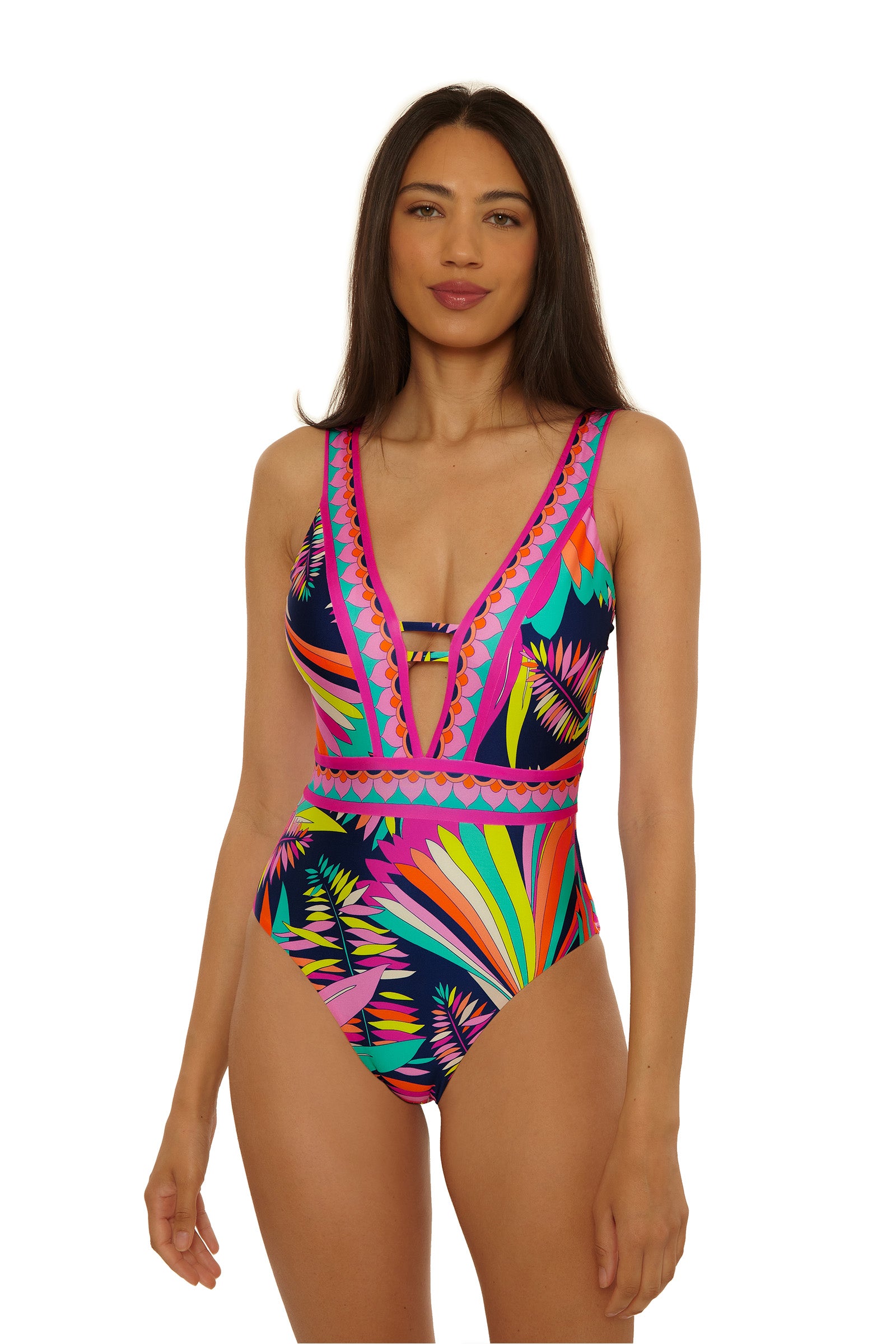 A woman with long dark hair wears the Paralia Border Plunge 1Pc, a colorful one-piece swimsuit featuring a deep V-neck and bold geometric and floral patterns in pink, blue, yellow, orange, and green on a white background.