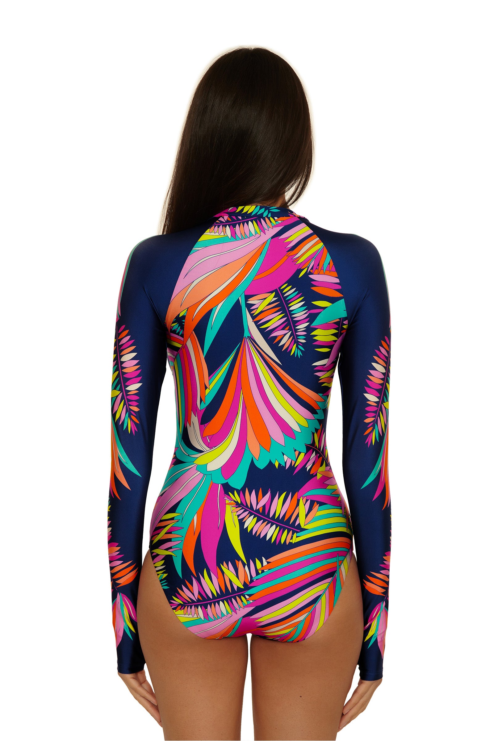 A woman with long dark hair, seen from the back, wears the Paralia Zip Up Paddlesuit—a long-sleeved swimsuit with a bold tropical leaf pattern on a dark background.