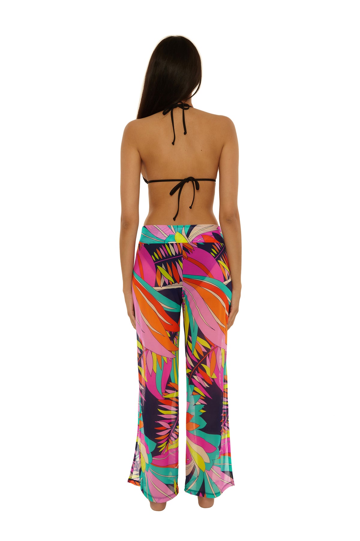 A woman with long brown hair, seen from the back, models the Paralia Mesh Swim Pant—a pair of brightly colored, tropical-patterned wide-leg pants—paired with a black halter bikini top against a plain white background.