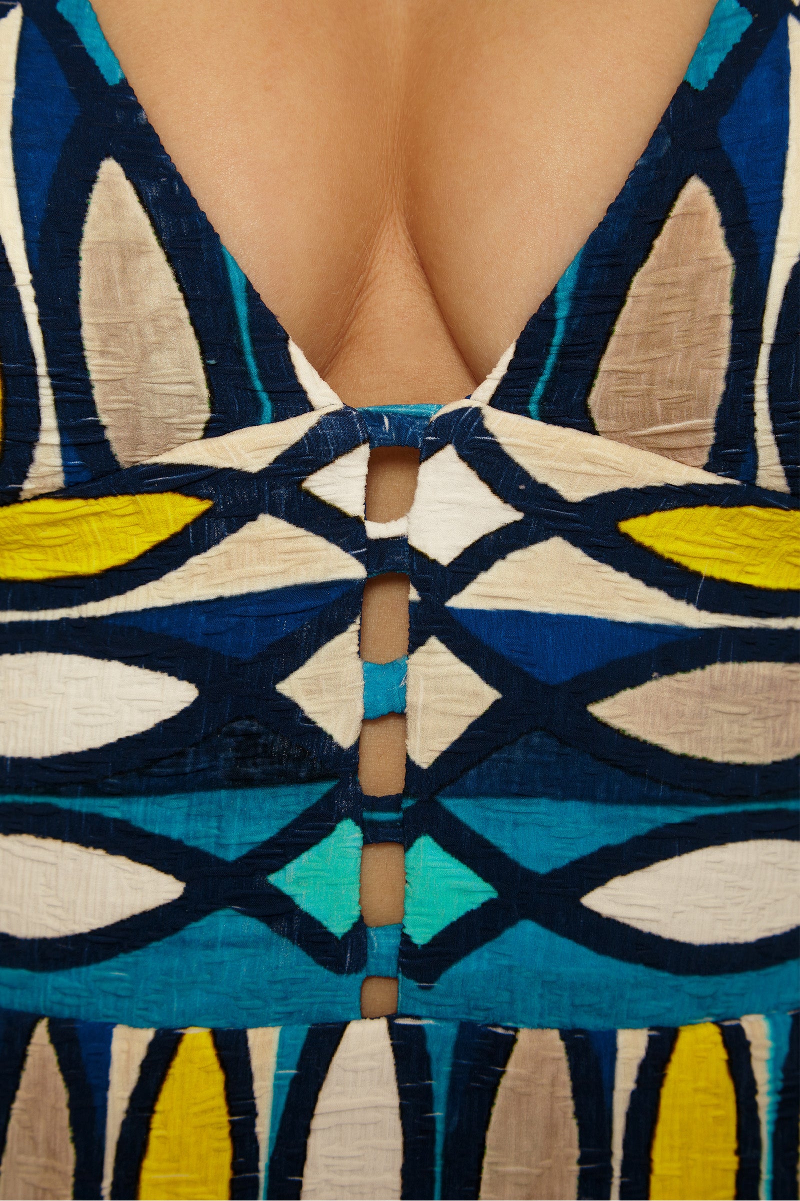 Close-up of a person wearing the Paros Empire Waist Maillot, a colorful swimsuit with blue, yellow, and cream geometric patterns, featuring a deep V neckline and central cut-out details.