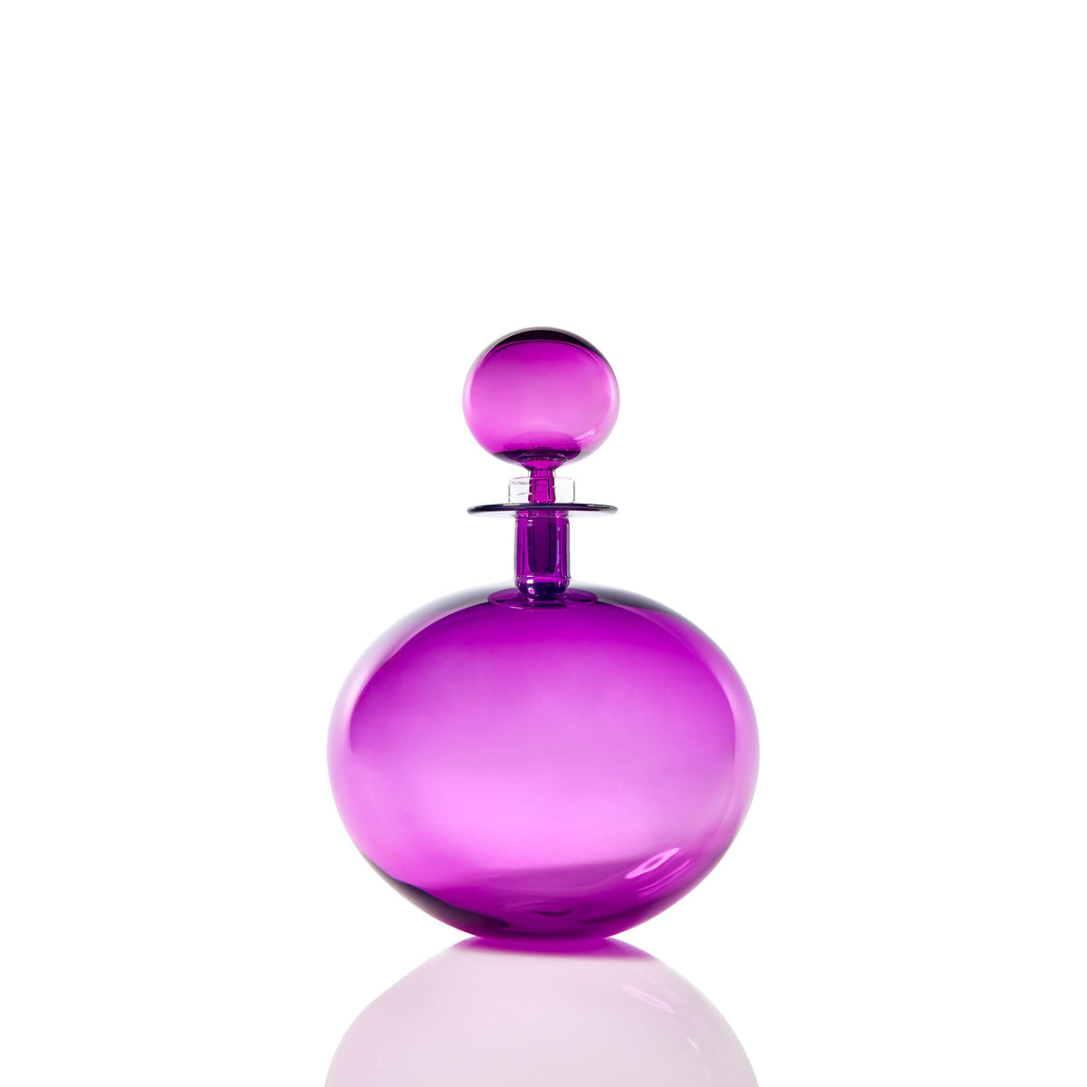 The Petite Low Round Decanter in ultraviolet glass features a round, glossy form with a matching spherical stopper, elegantly set against a white background with its faint reflection below.