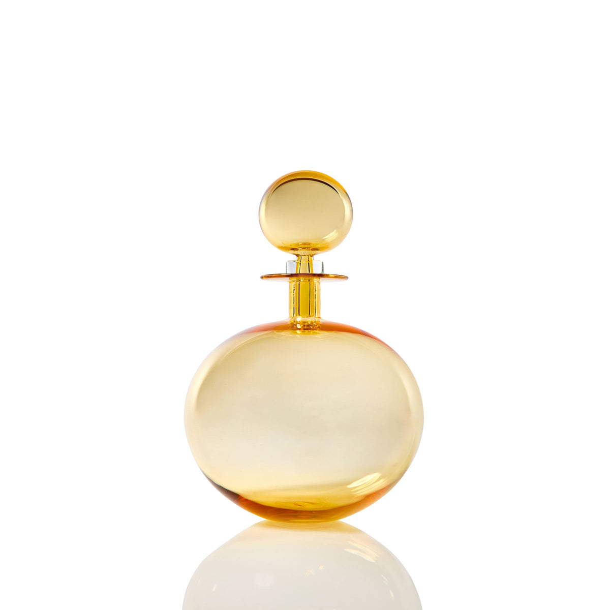 The Petite Low Round Decanter in whiskey, featuring an elegant silhouette and matching spherical cap, is showcased against a white background with a subtle reflection below.